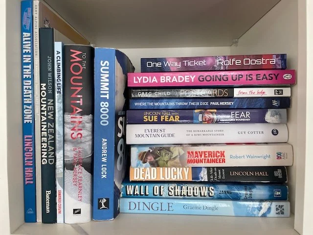 a bookshelf containing a large stack of books of New Zealand and Australian mountaineers