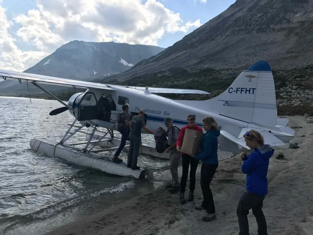hikers unloading the floatplane by the waters edge of the wilderness lake