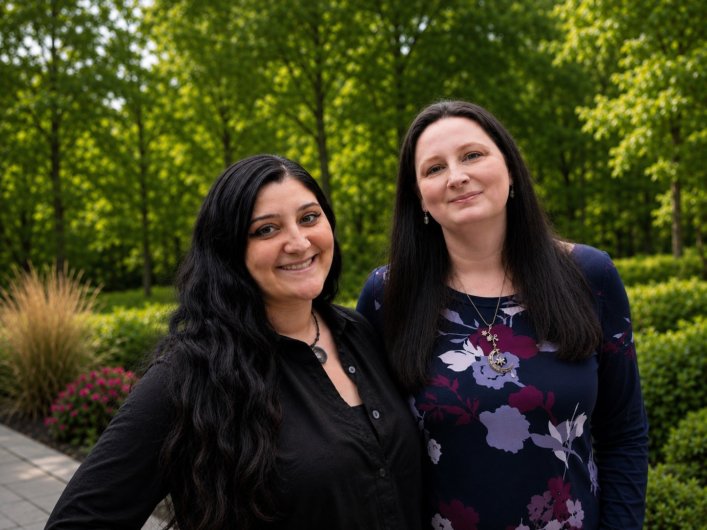 Two women stand outdoors in front of a lush green background, smiling and posing for a photo.