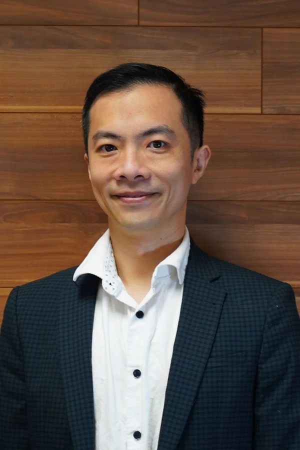 Portrait of a smiling Asian man in a suit with a wooden wall background.