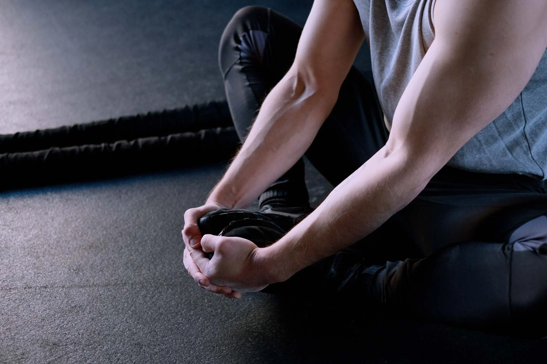 Person sitting on the floor tying their shoelace, with rowing ropes in the background.