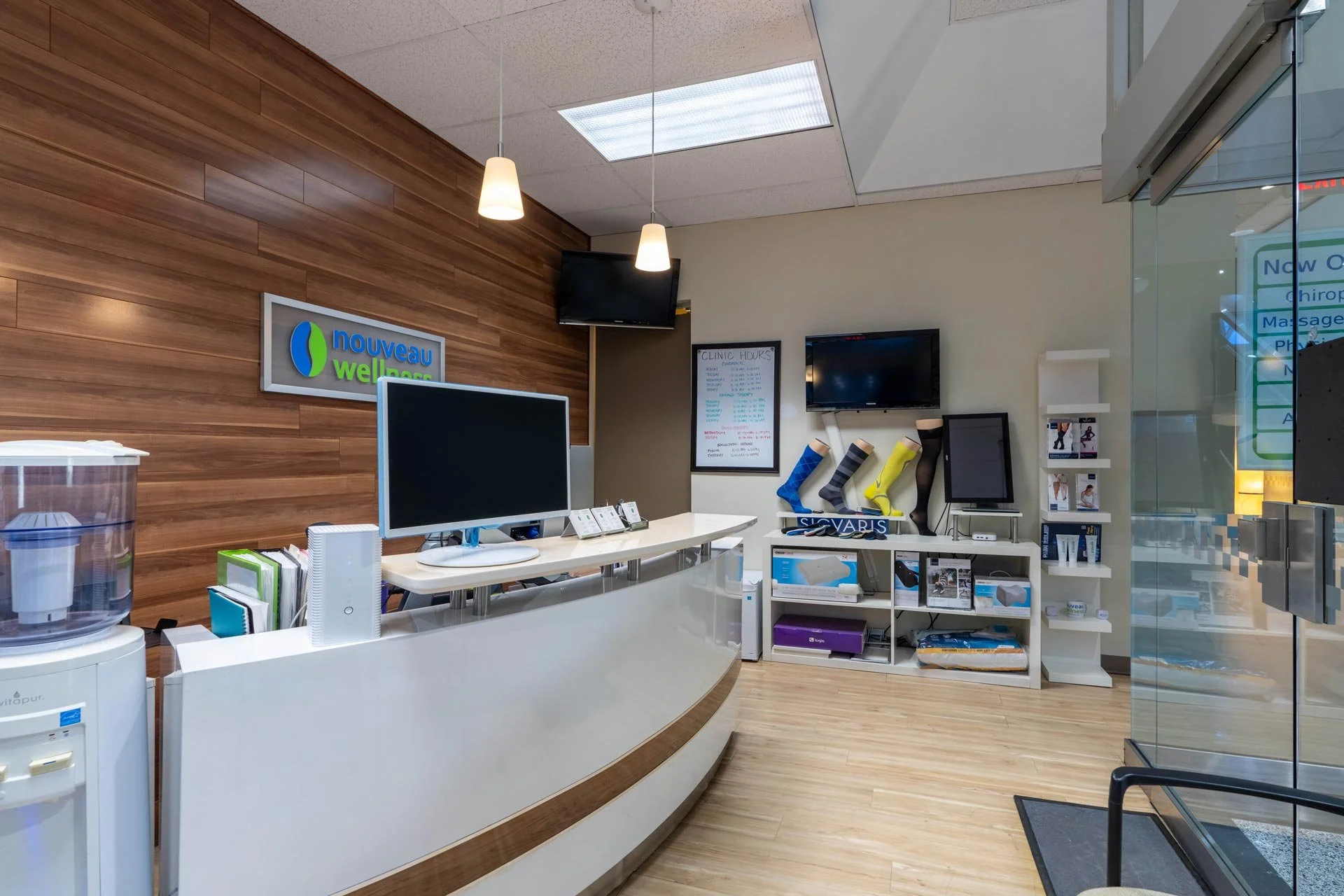 Interior of a wellness clinic with a reception desk, a wooden accent wall, monitors, and shelves displaying health and wellness products.