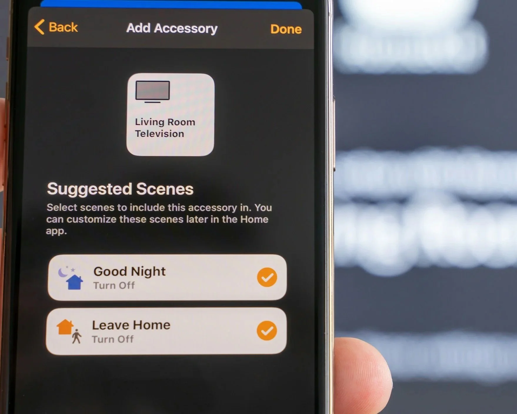 Smartphone screen displaying a home automation app with options to add a living room television and suggested scenes to turn off the TV and turn off the home when leaving.