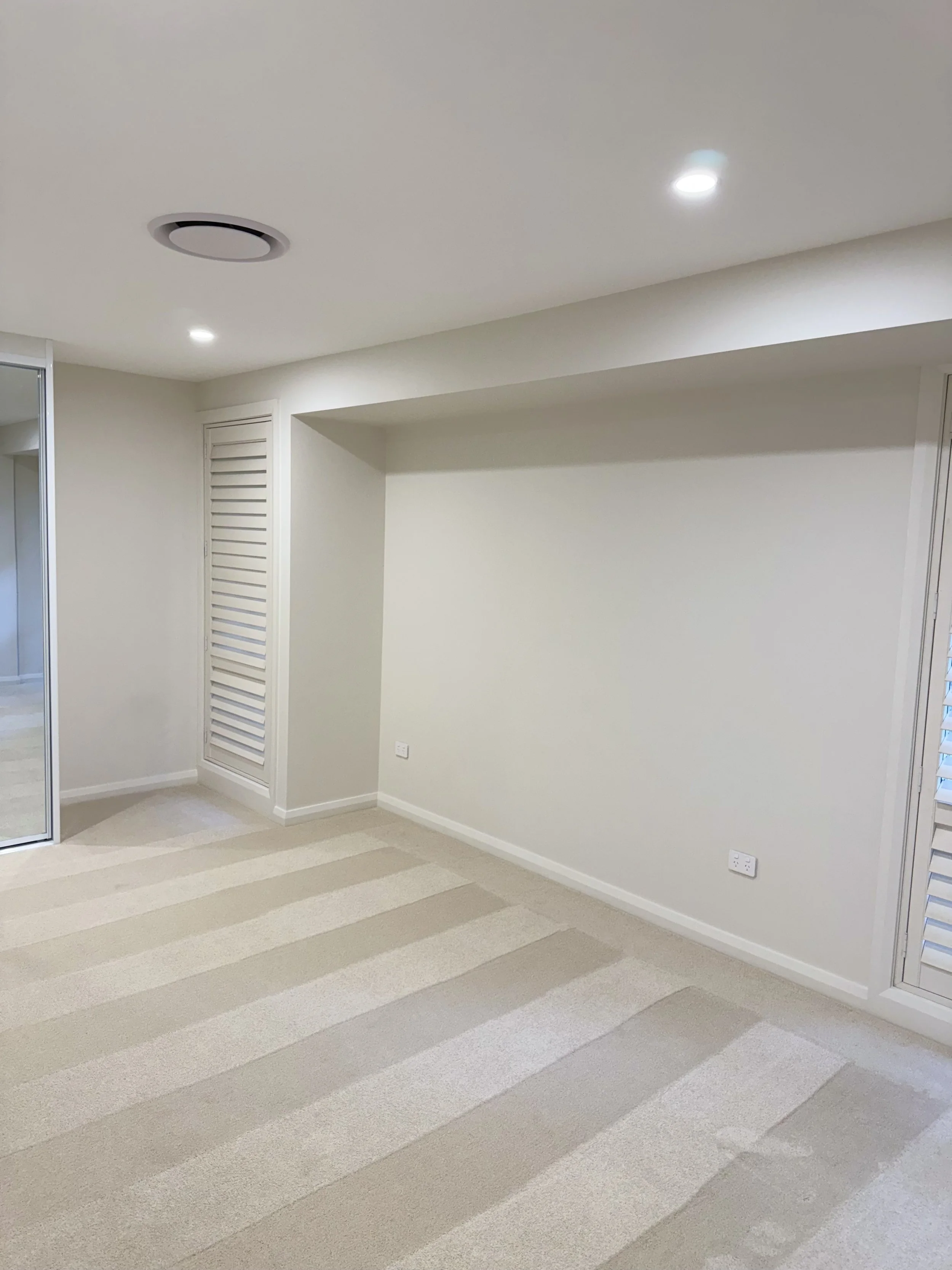 Interior room with white walls, beige carpet with striped pattern, closet doors, electrical outlets, and ceiling lights.