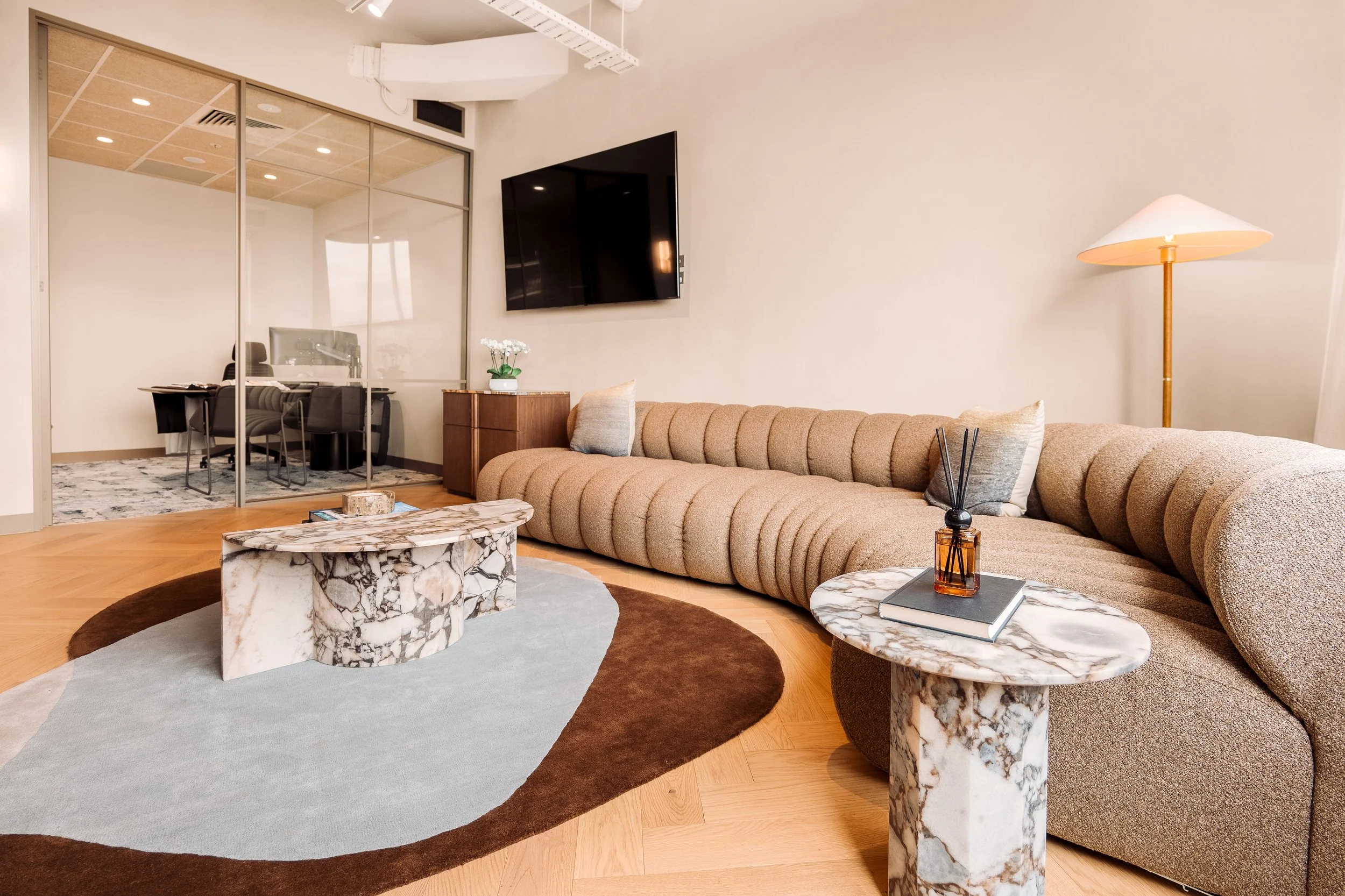 A modern living room with a beige upholstered sectional sofa, marble side tables, and a dark brown and beige rug.