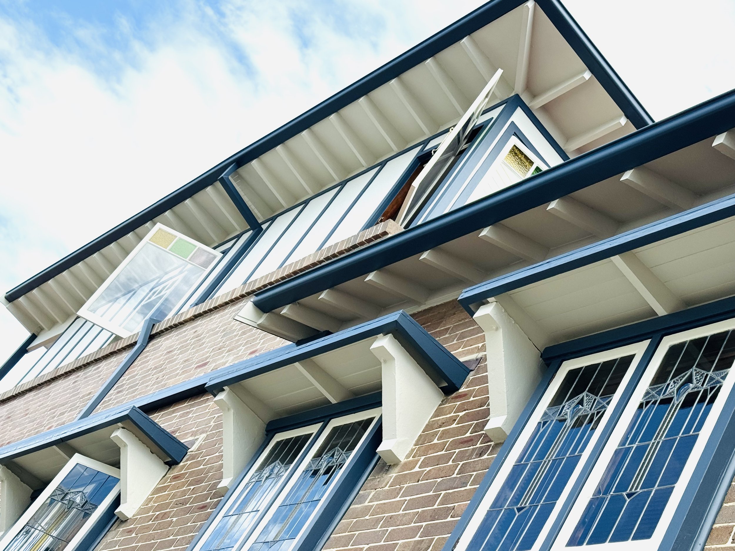 Low-angle view of a modern multi-story residential building with brick and blue framed balconies, set against a partly cloudy sky.