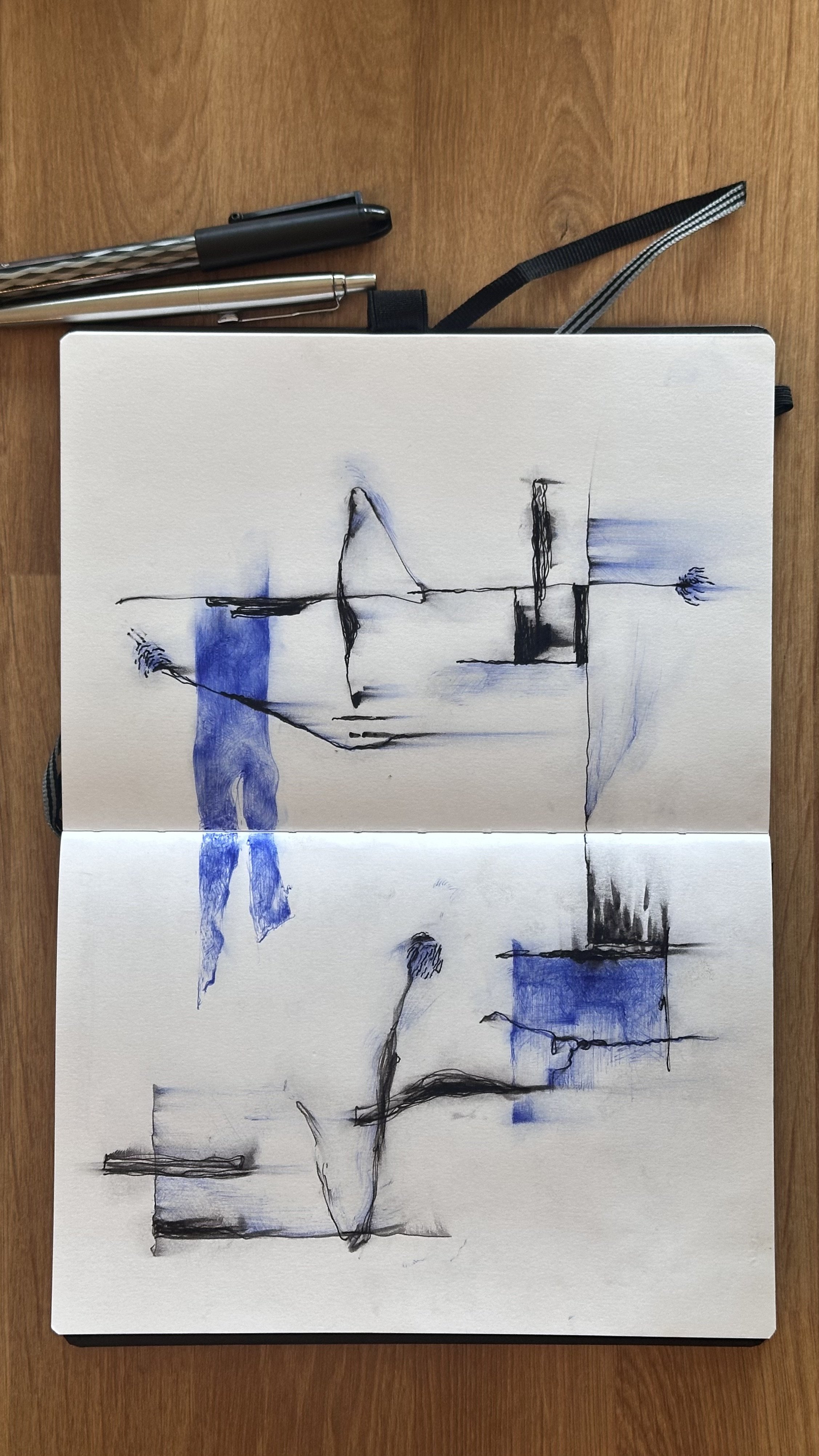 An open sketchbook with an abstract ink and watercolor drawing in black and blue on a wooden surface, with three pens and a mechanical pencil placed above it.