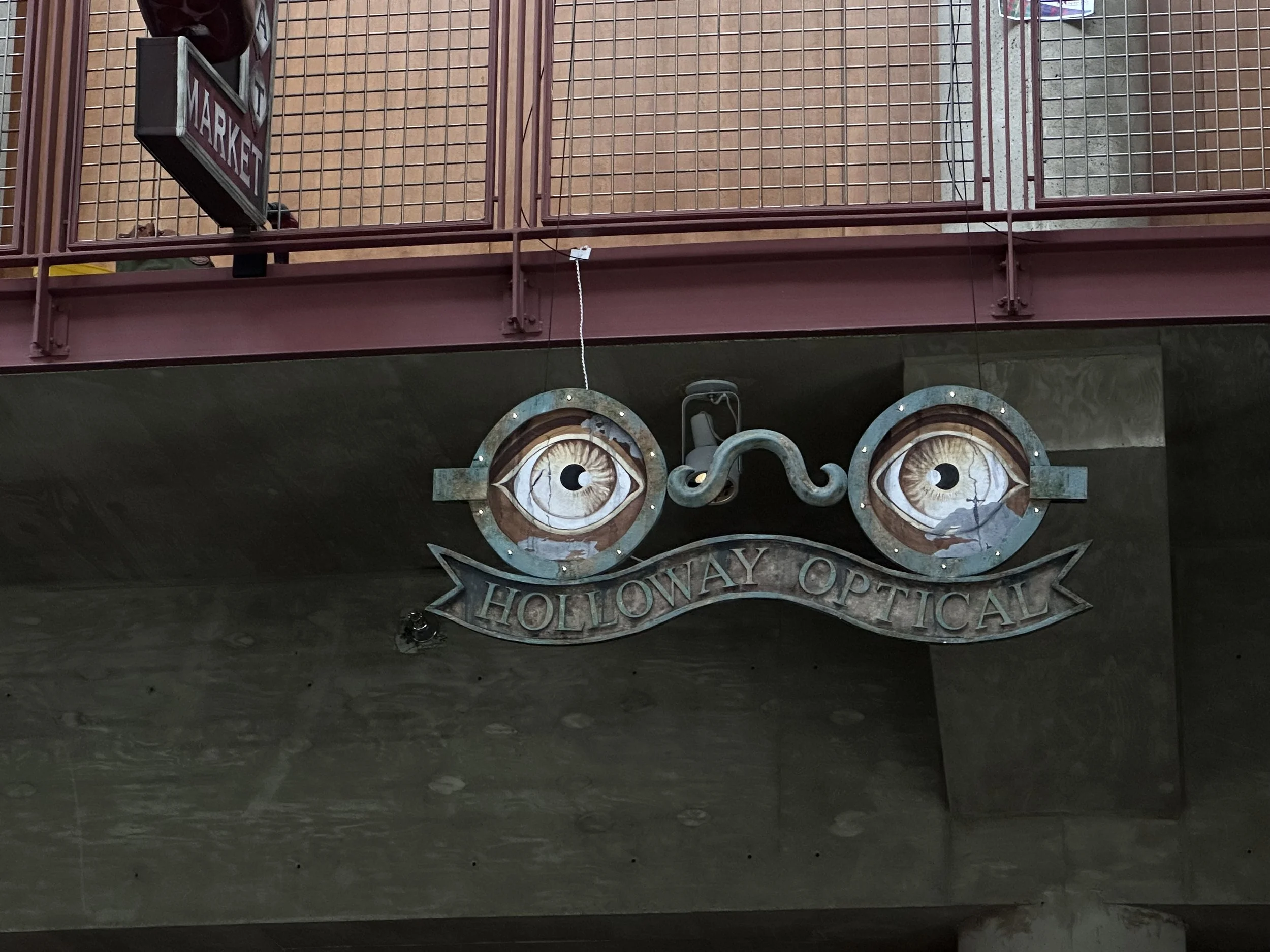 Entrance sign for Hollywood Optical during daytime, with decorative eyes on the wall below.