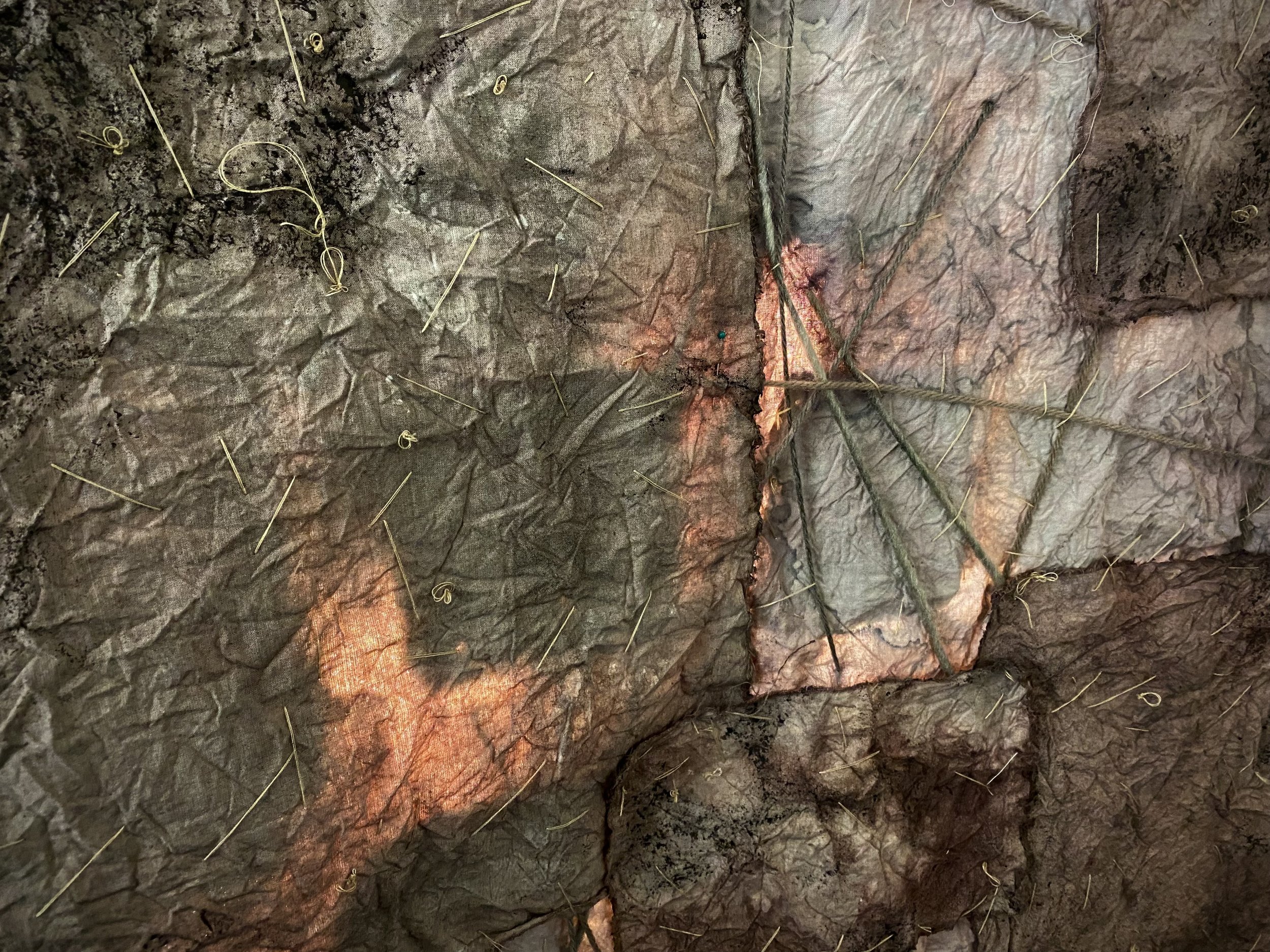 Close-up of a rock face with numerous pins and small pieces of string or wire attached, some of which are illuminated with a warm light.