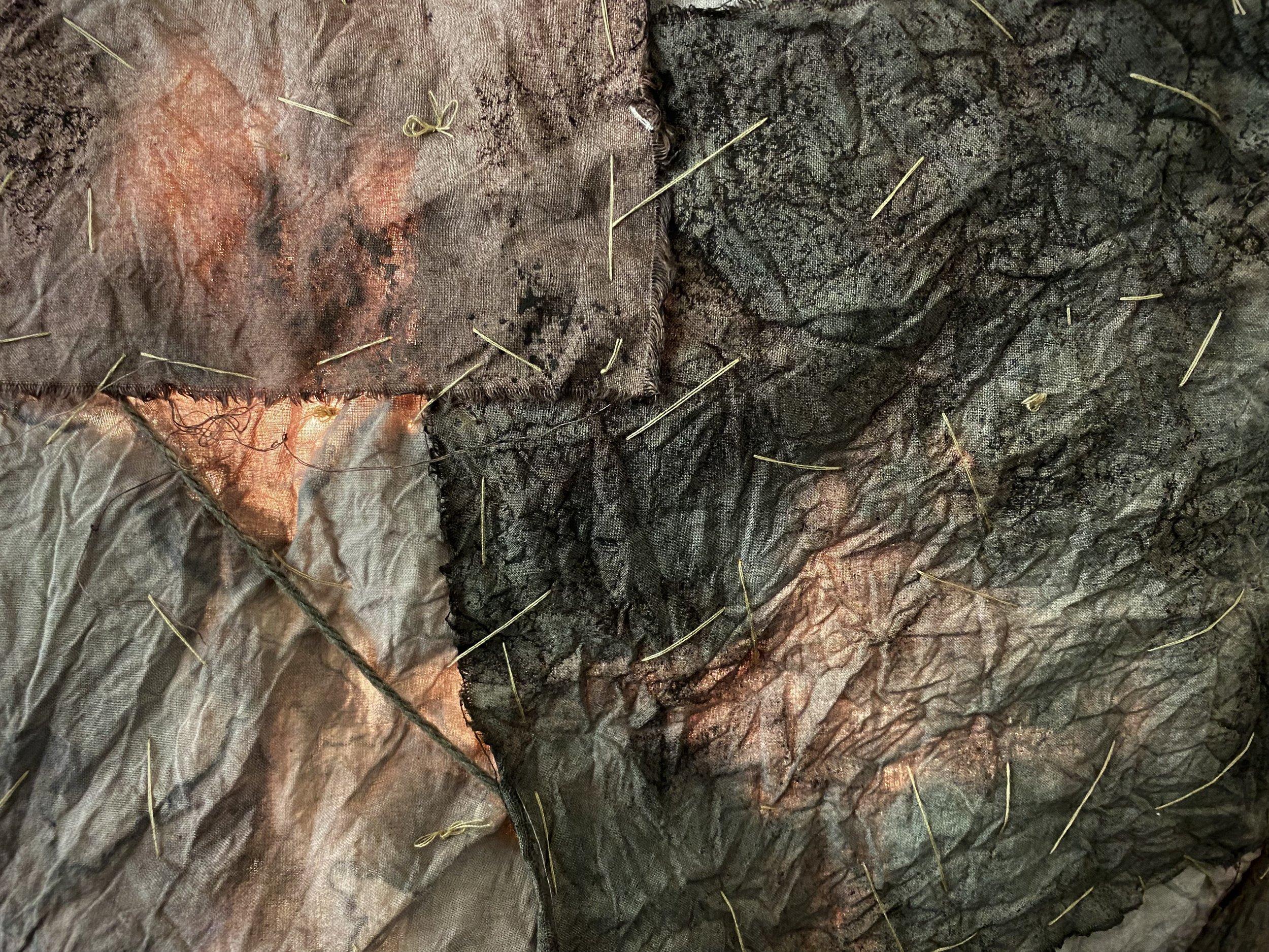 Close-up of several layers of black and brown fabric with scattered small pins on them.