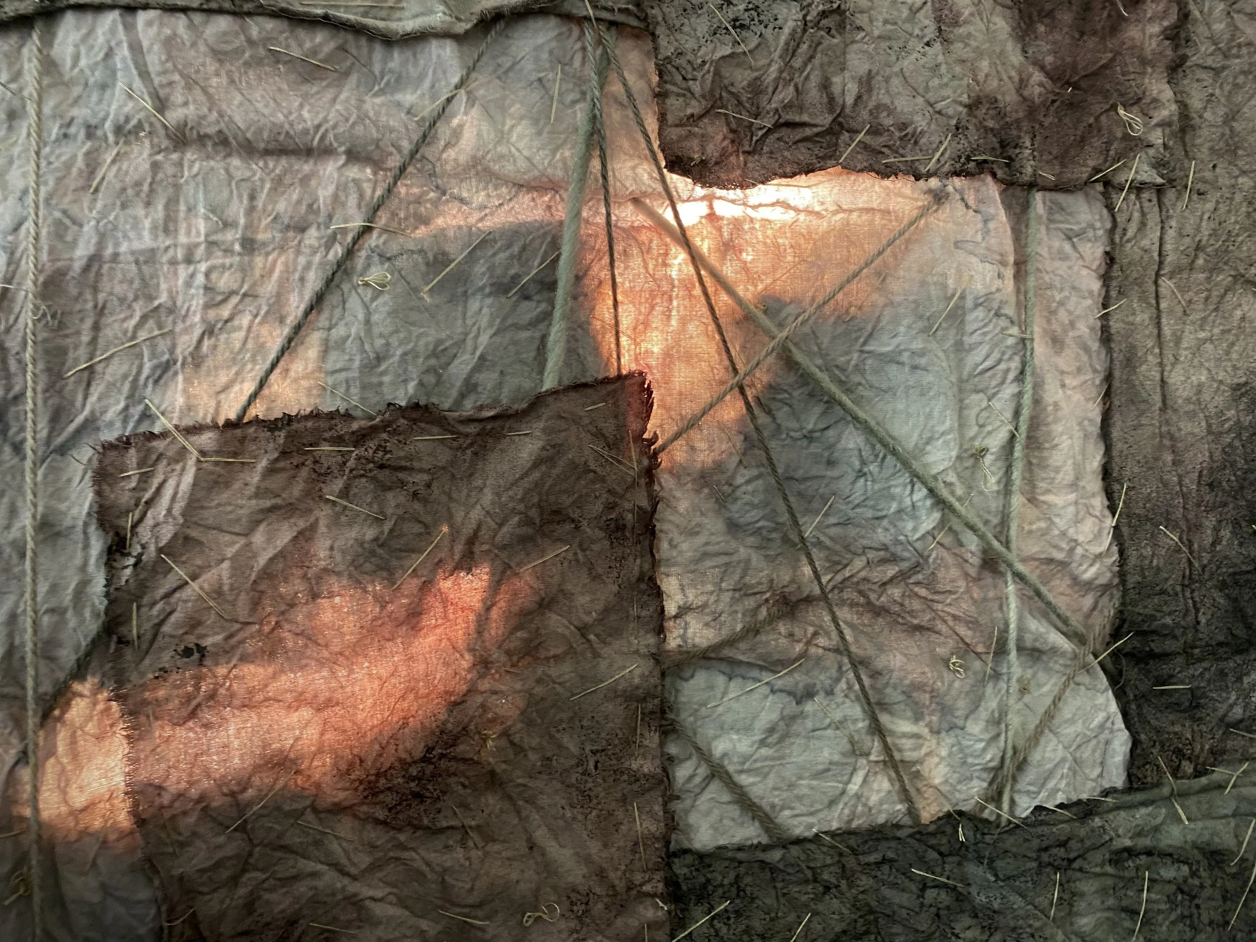 A close-up view of a rock wall with large, uneven rocks held together by ropes and stakes, with some areas illuminated by warm, orange-colored lighting.
