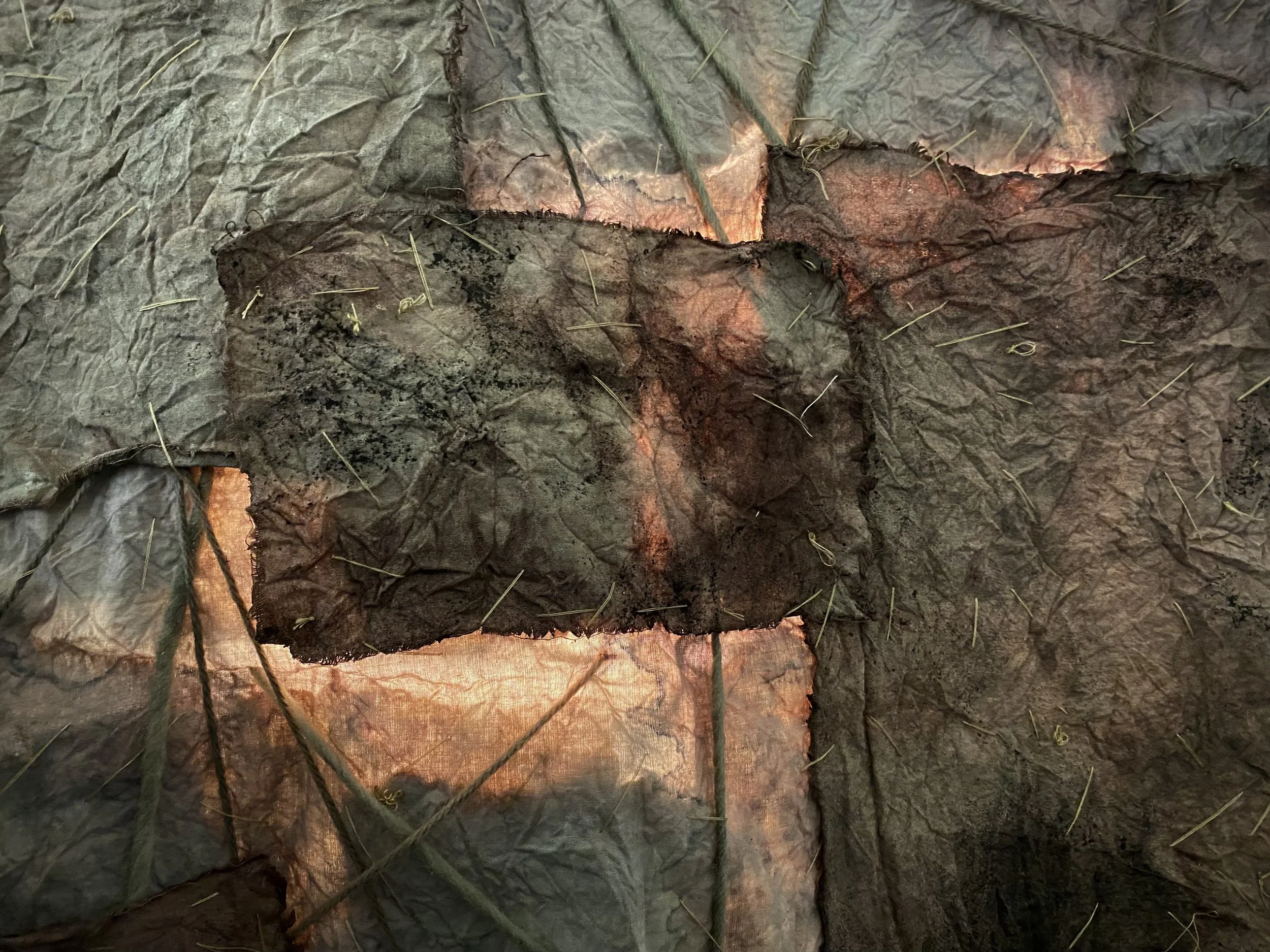 Close-up of a damaged piece of blackened, wrinkled fabric, revealing red glowing embers underneath.