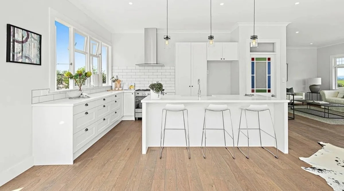 Renovated villa kitchen in Tawharanui Peninsula featuring white shaker cabinetry, stone benchtops and timber flooring.