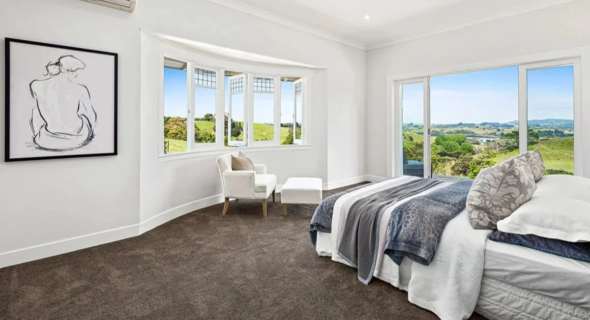 Master bedroom in renovated Matakana villa with bay window seating and expansive rural views across the countryside.