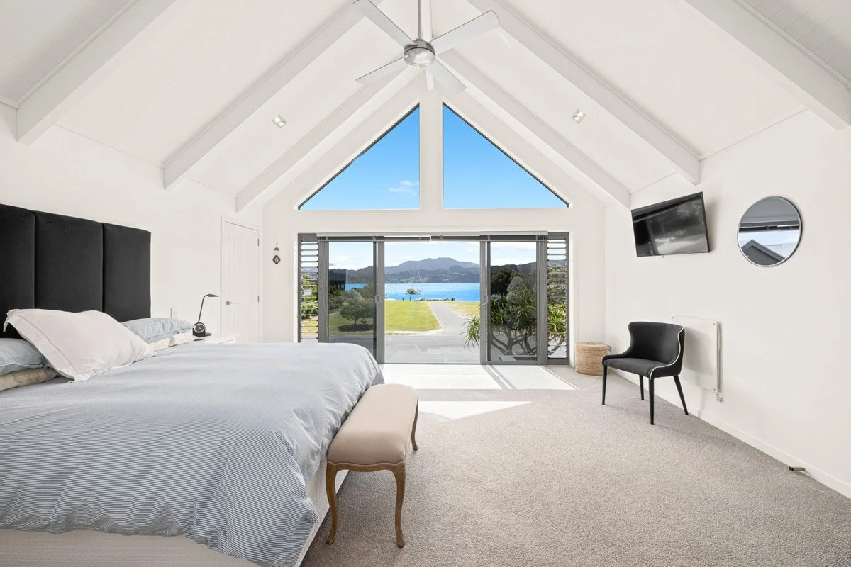 Master bedroom with vaulted ceilings, large glazing and harbour views in an architectural Omaha waterfront home.