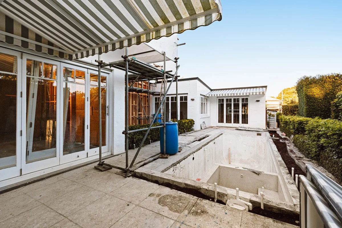 Poolside outdoor living area under construction with new glazing, plastered exterior walls and landscaping preparation in Auckland.