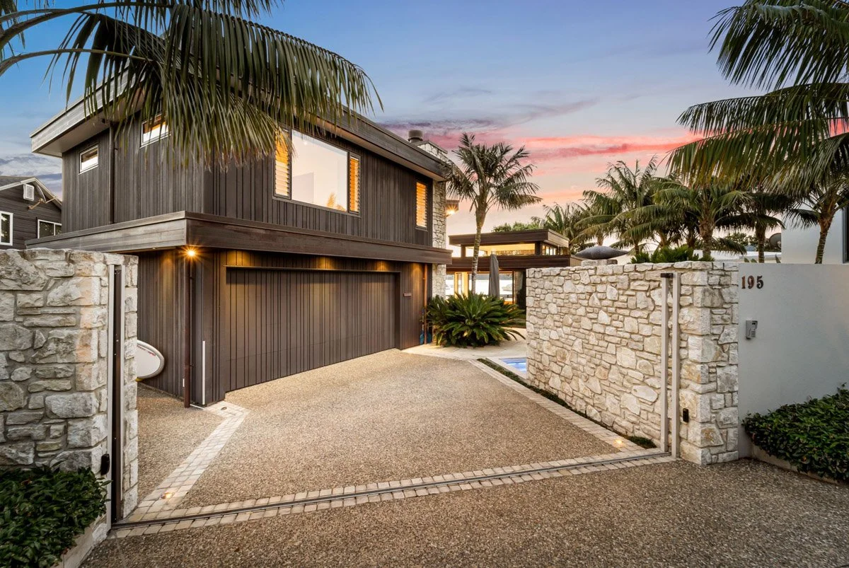 Street frontage of a contemporary Omaha waterfront home featuring dark timber cladding, natural stone walls and architectural detailing.