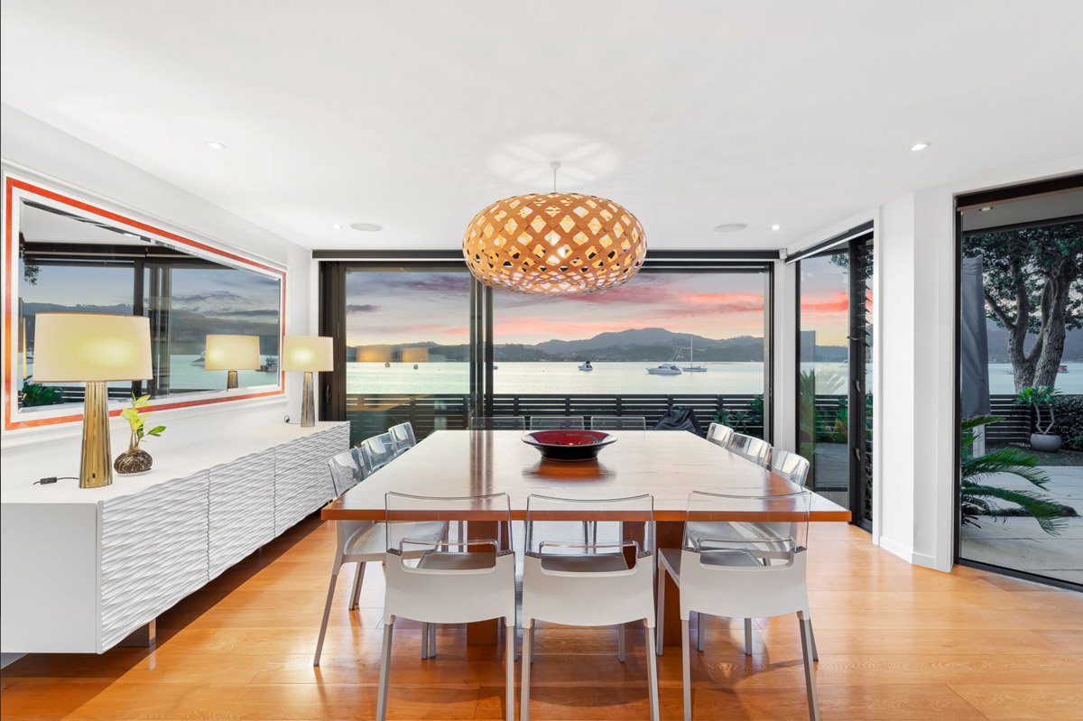 Dining space with floor-to-ceiling glazing and uninterrupted harbour views in a luxury Omaha waterfront home.