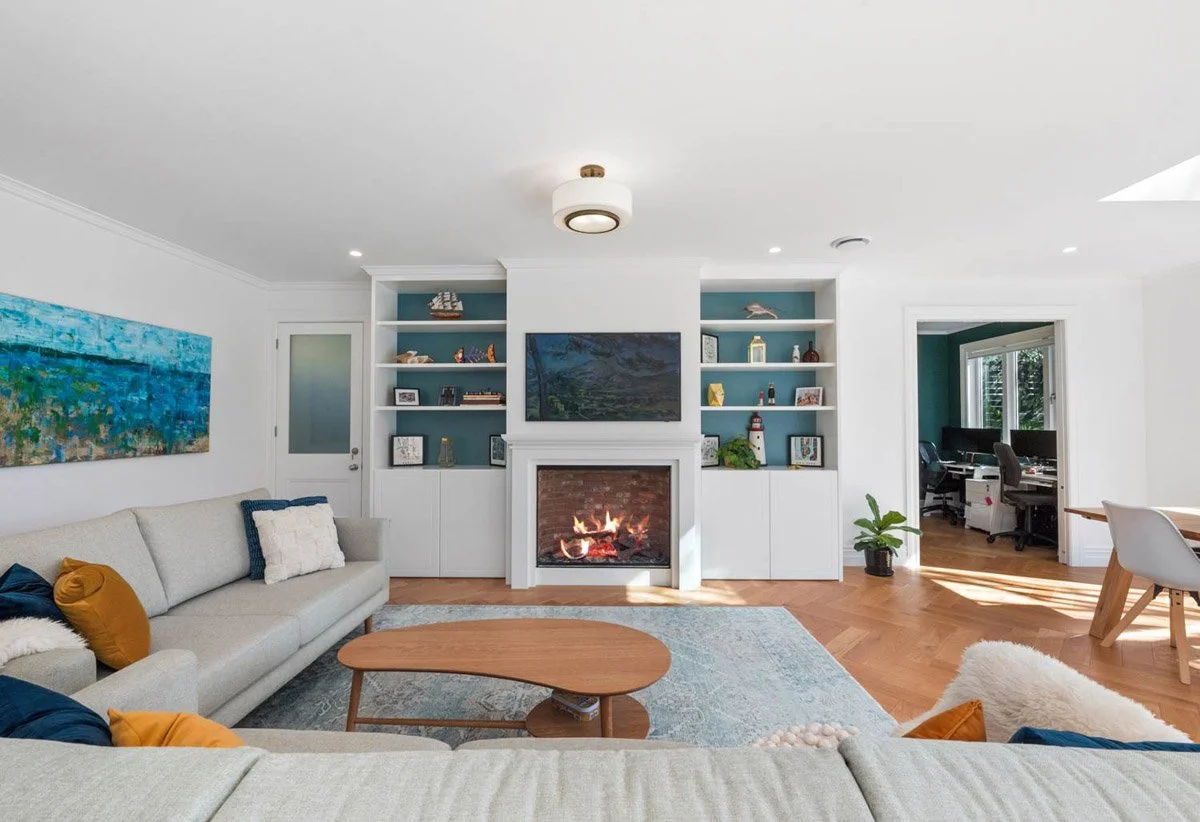 Open-plan living area with fireplace, custom cabinetry and timber flooring in extensively renovated Devonport home.
