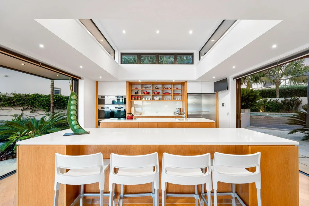 Architectural kitchen with timber cabinetry, oversized island and harbour views in a luxury Omaha waterfront home.