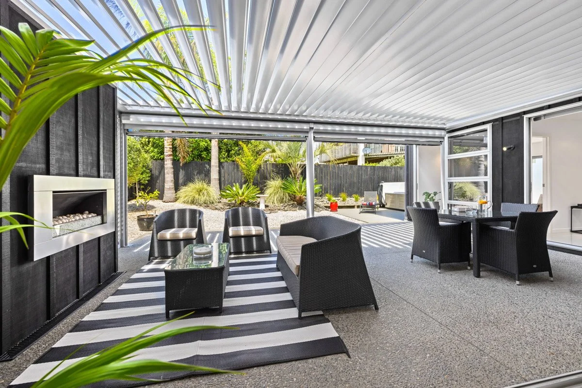 Covered outdoor entertaining area with louvre roof system and outdoor fireplace in an Omaha coastal home.