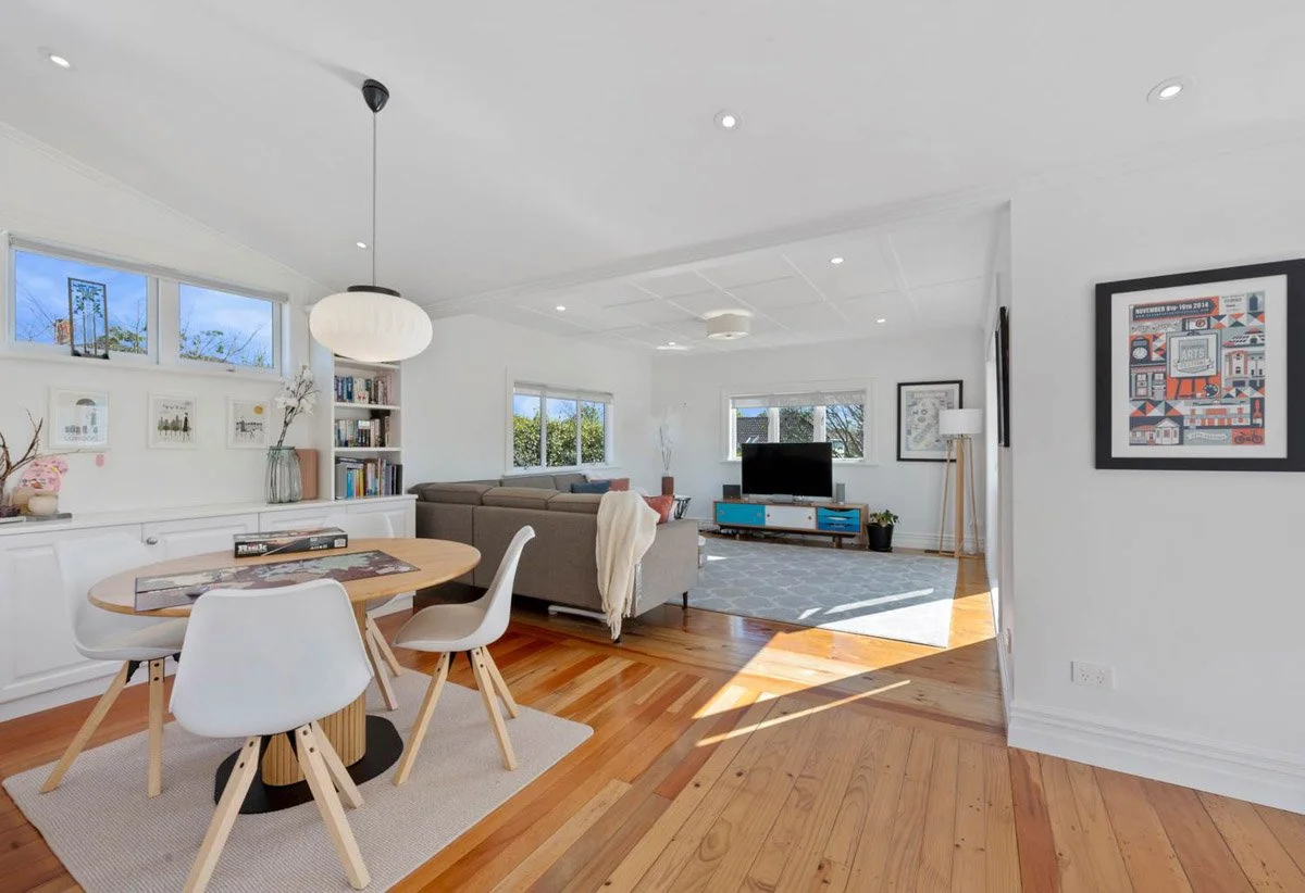 Family lounge with restored timber flooring and natural light in renovated Devonport villa.