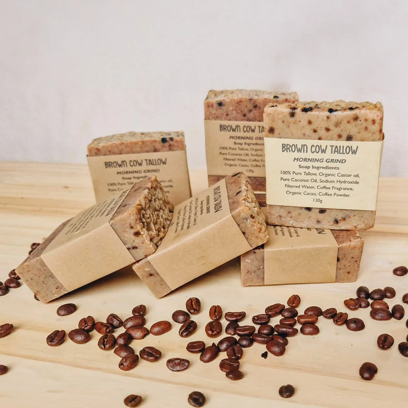 Handmade soap bars labeled 'Brown Cow Tallow Morning Grind' on a wooden surface, surrounded by scattered coffee beans.