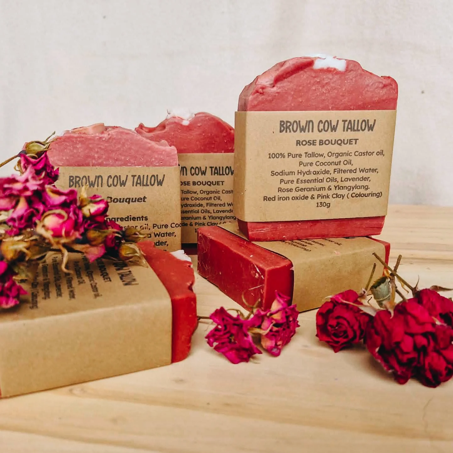 Three handmade soap bars labeled "Brown Cow Tallow Rose Bouquet" with dried pink and red flowers around them.