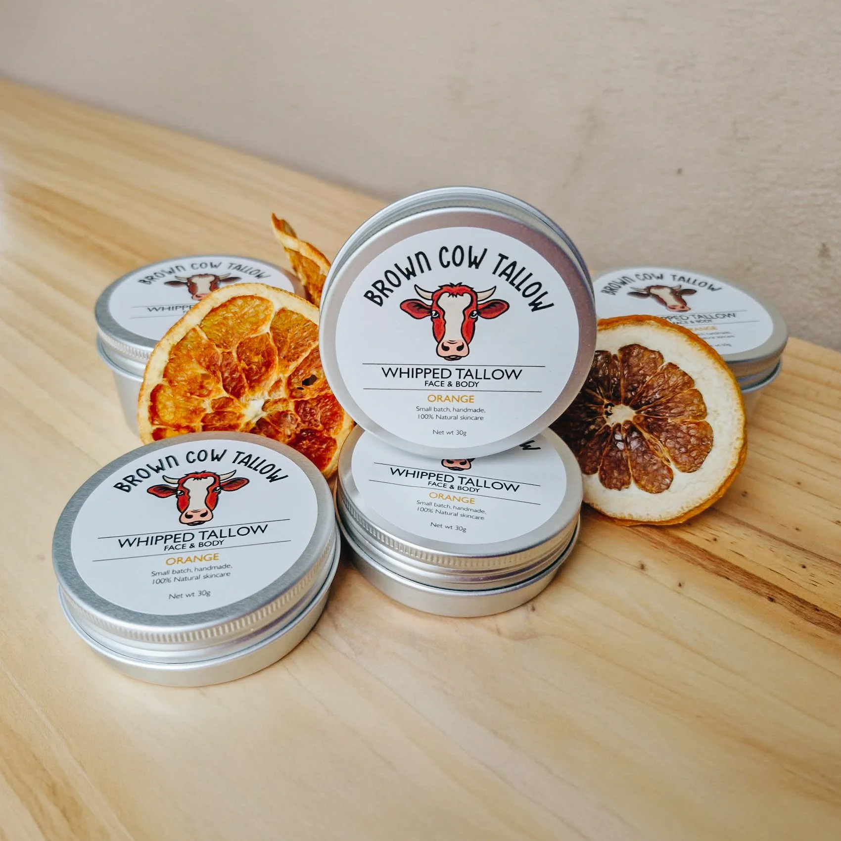 Multiple containers of Brownd Cow Tallow whipped skincare cream with dried orange slices on a wooden surface