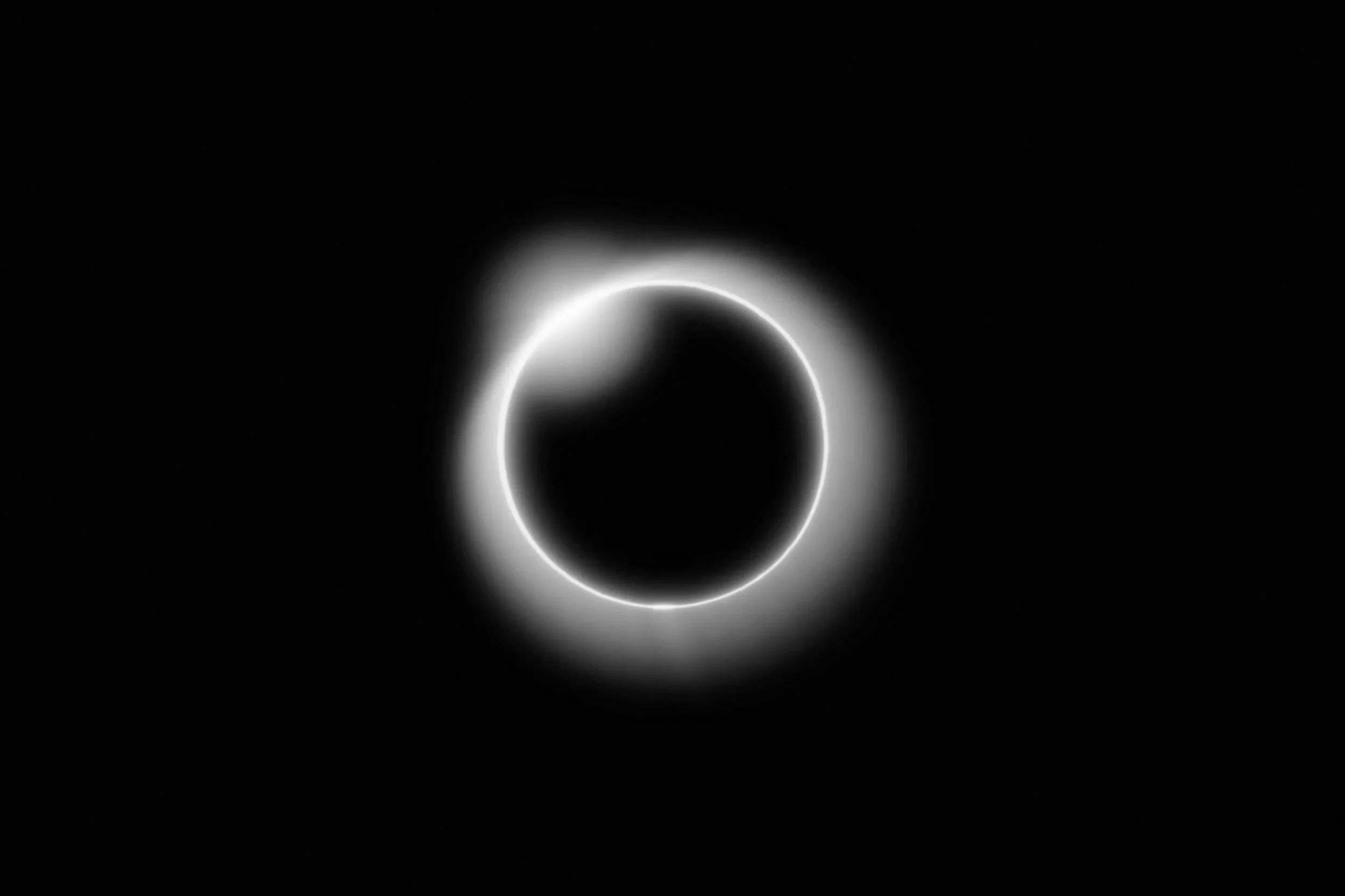 Black space with a bright ring of light around a dark circle, resembling a solar eclipse.