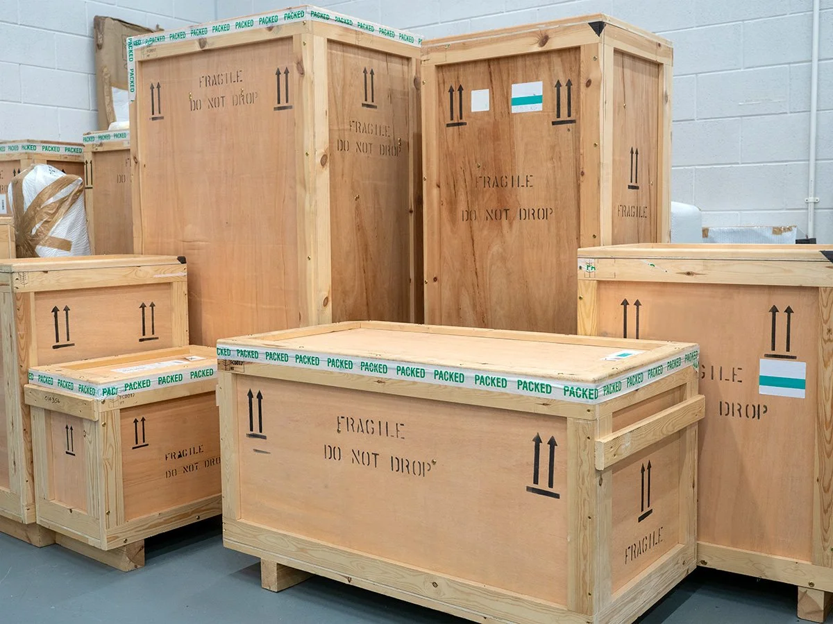 Several large wooden shipping crates with 'FRAGILE' and 'DO NOT DROP' marked on them, stored indoors on a warehouse floor.