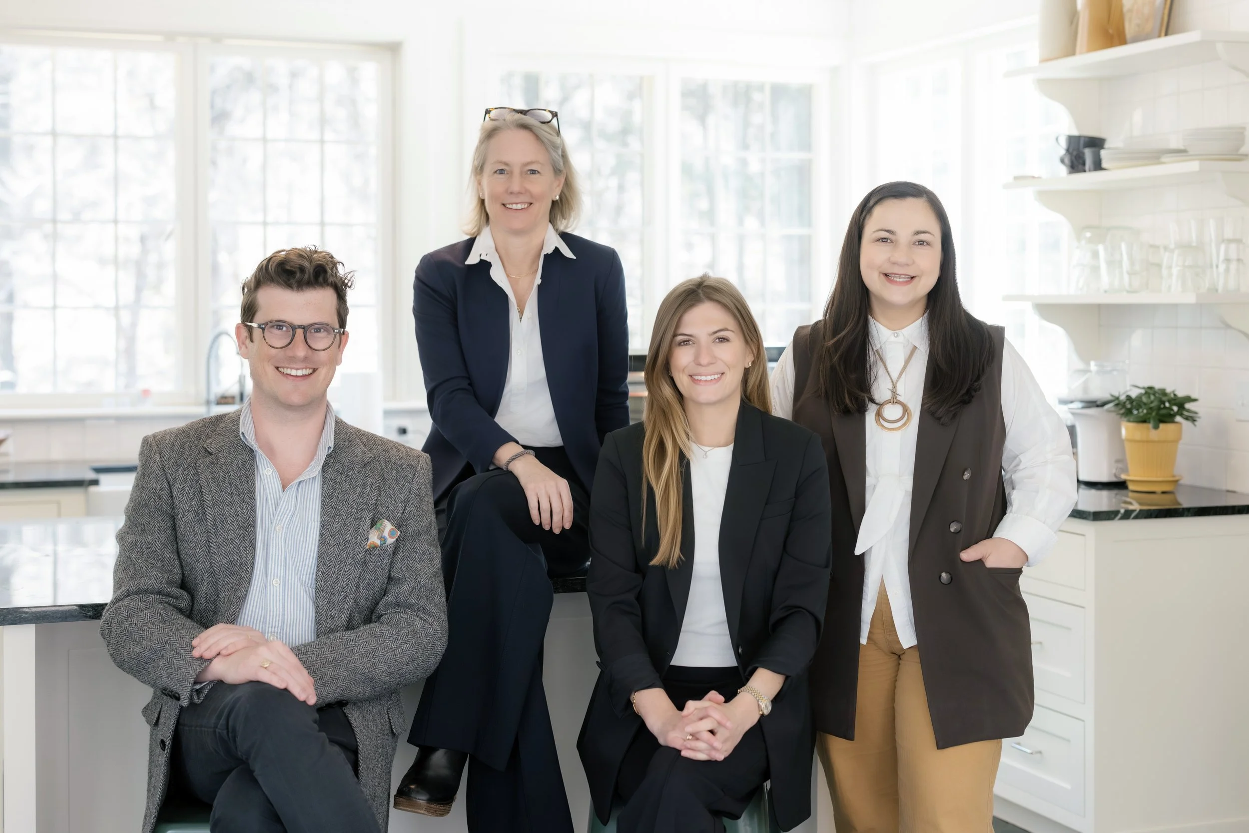 Group of five diverse professionals in business attire smiling in a bright kitchen or office space.