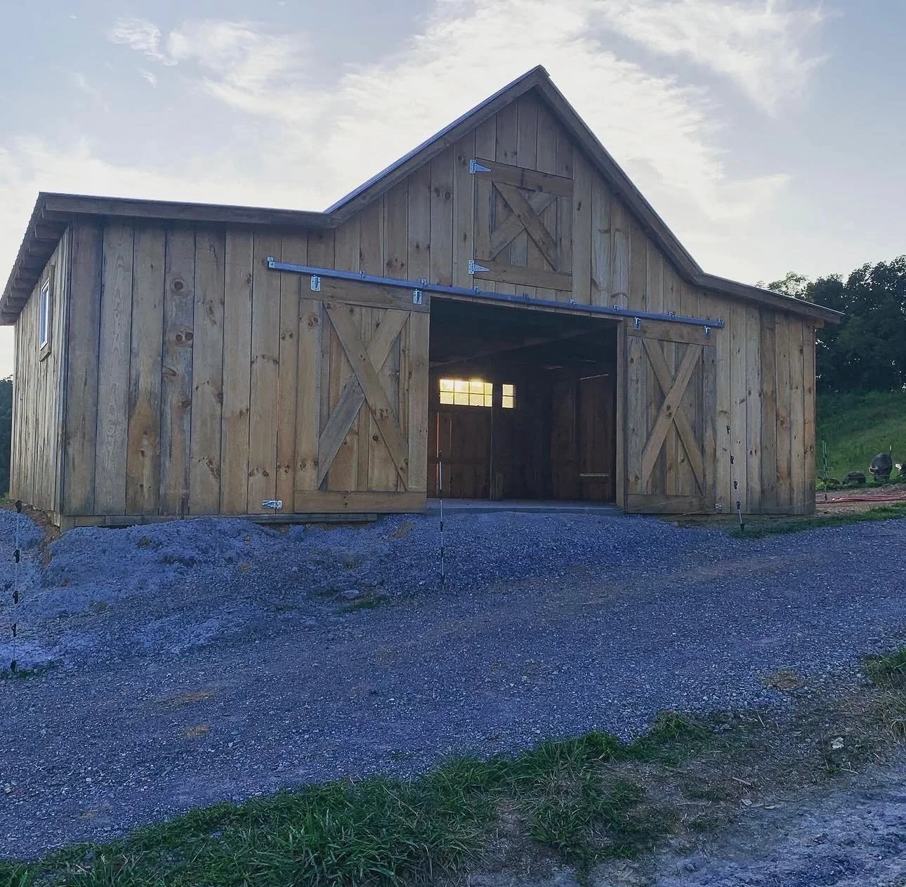 A wooden barn under construction with sliding doors, located in a rural area during the daytime.