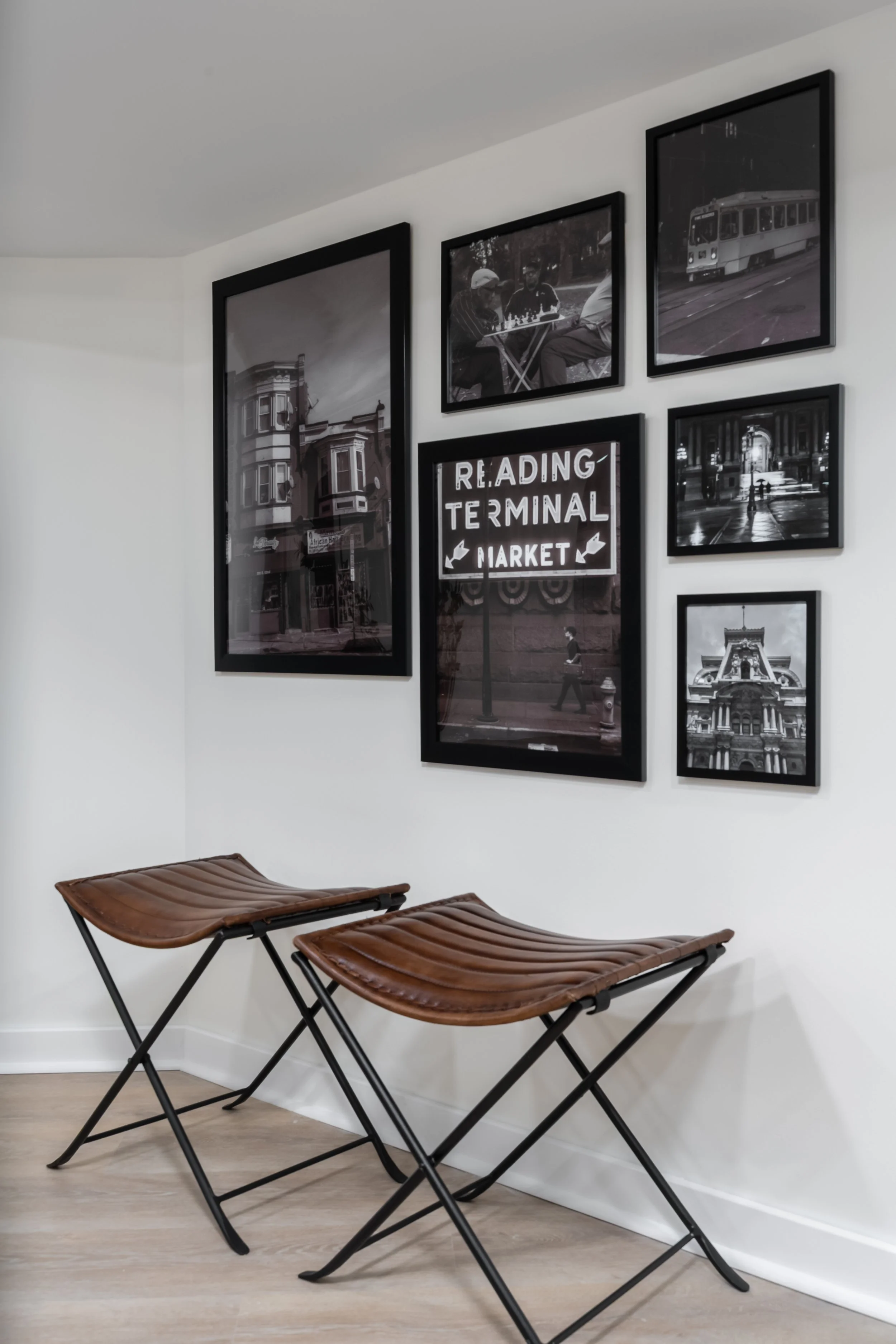 Two brown leather benches with black metal frames placed against a white wall, which displays a gallery of black-and-white photographs and a sign that reads 'Reading Terminal Market'.