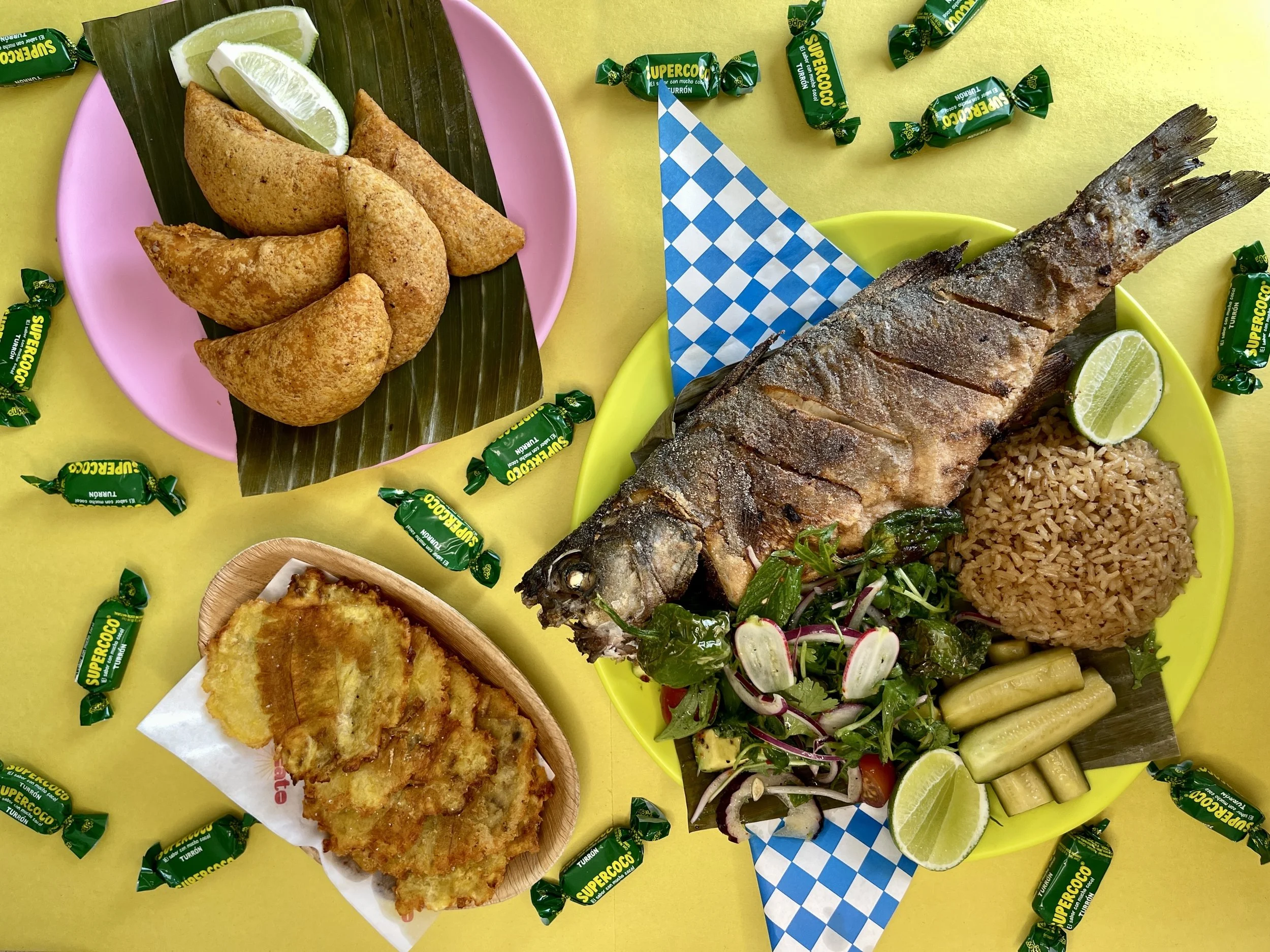 A plate of fried fish with coconut rice and a plate of empanadas in a colorful background.