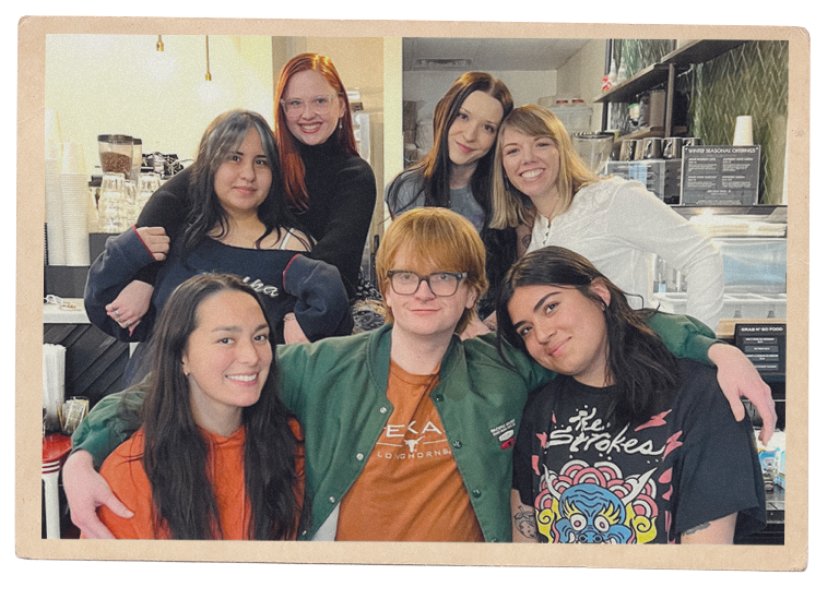 Group of seven young people smiling and posing together in a coffee shop.