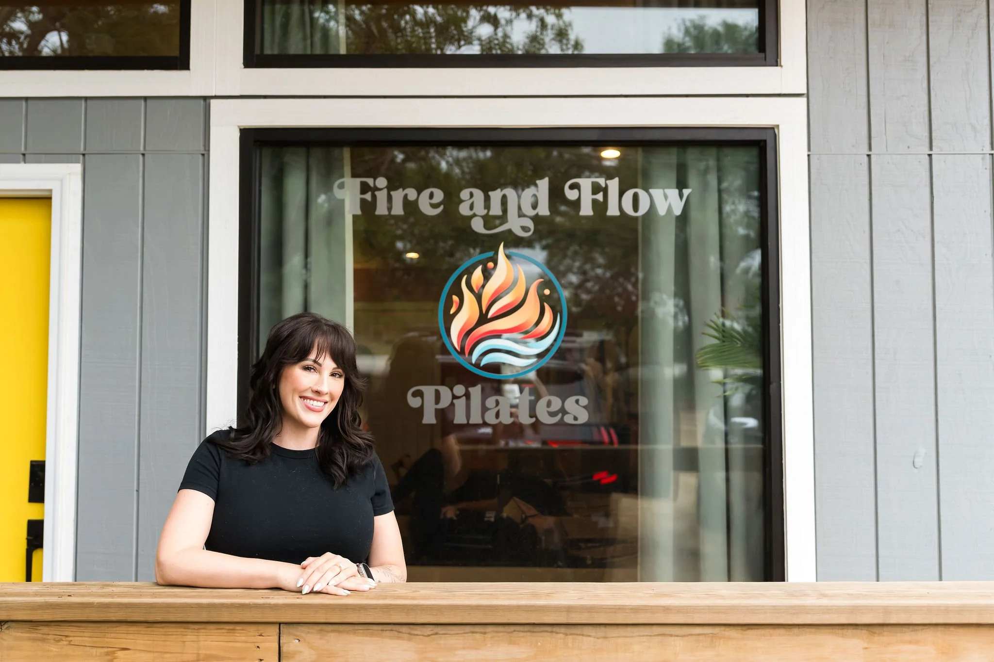 Woman with brown hair smiling, standing outside a restaurant called Fire and Flow Plates, with a wooden counter in front of her.