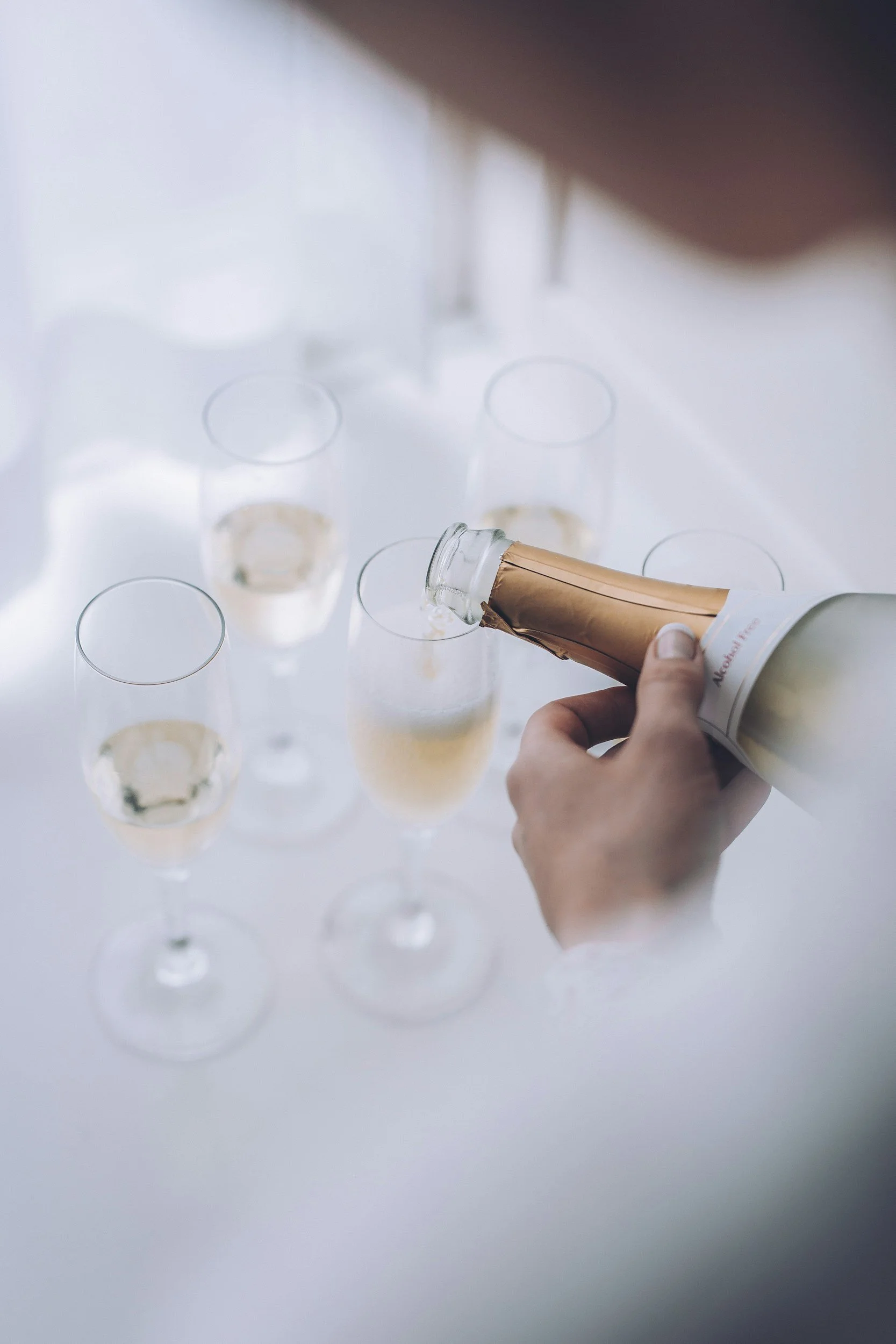 Close up of person pouring champagne into flutes on table with white table cloth