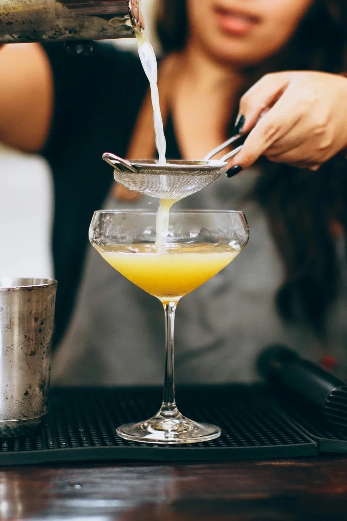 Close up of female bartender pouring yellow drink into coup glass