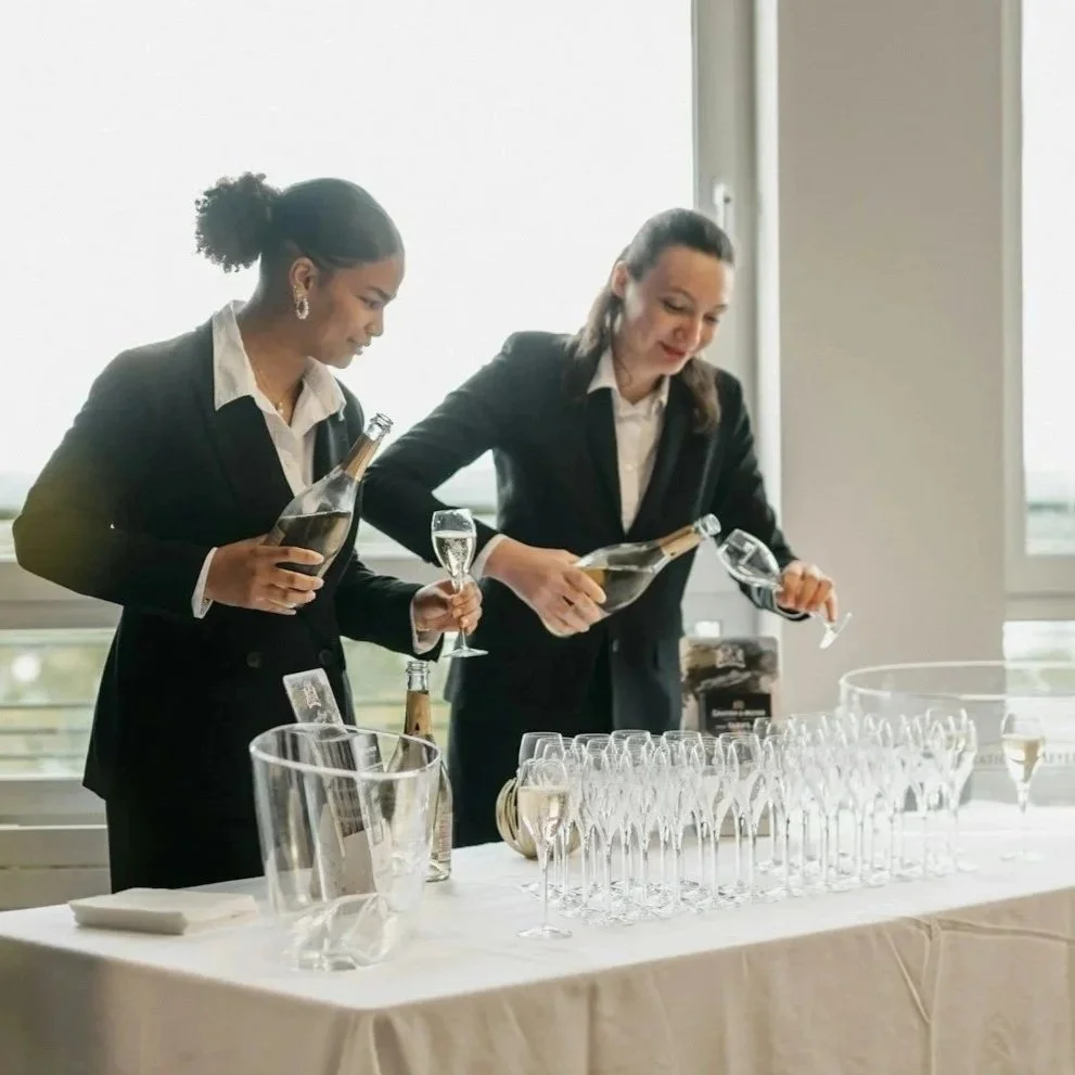 Two servers prepping and pouring drinks at a table full of glasses