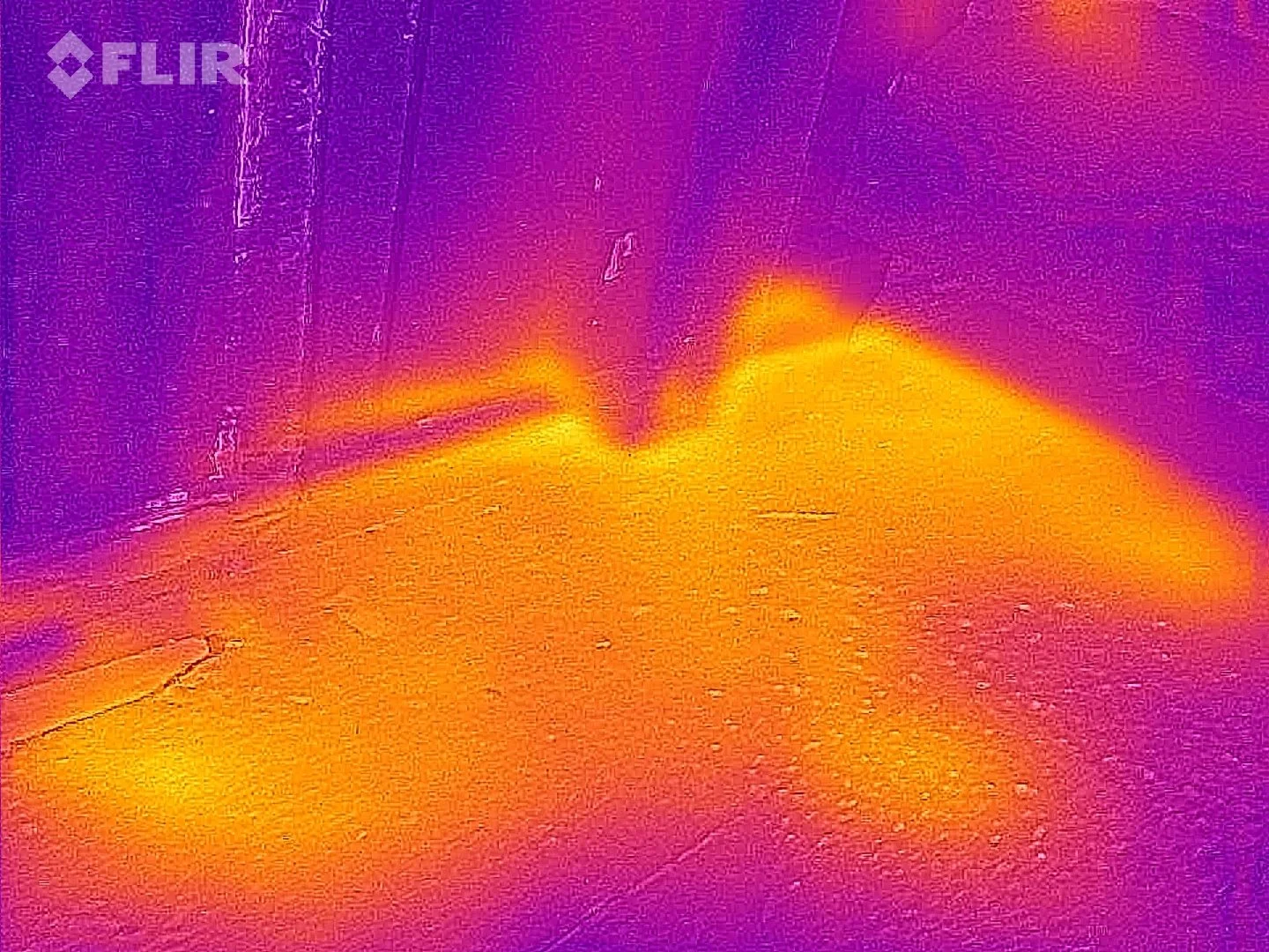 Thermal image of a corner with a door, showing the door's lower edge and a portion of the floor, with color indicating heat levels.