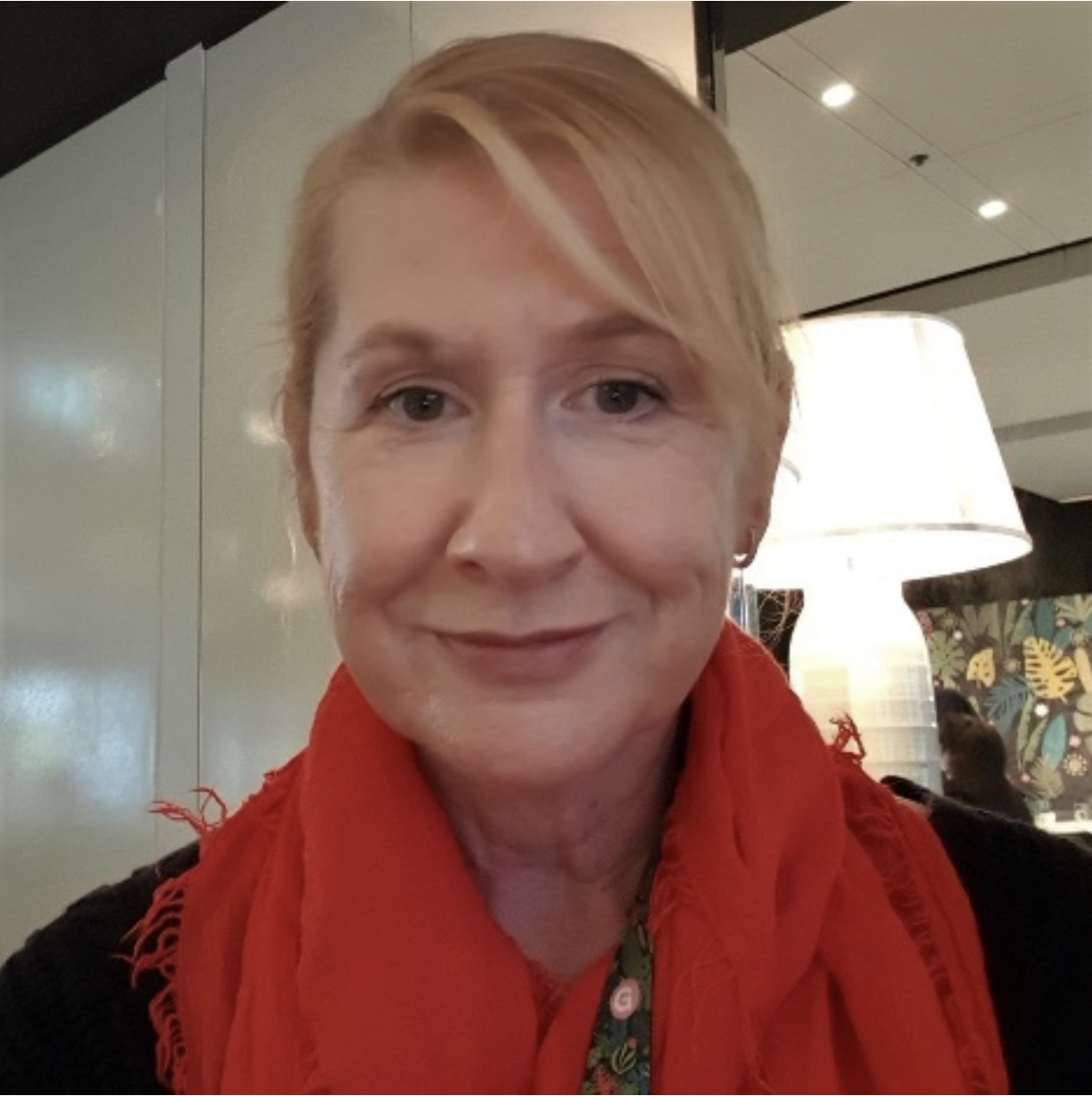 A woman with short blonde hair smiling, wearing a red scarf and black top