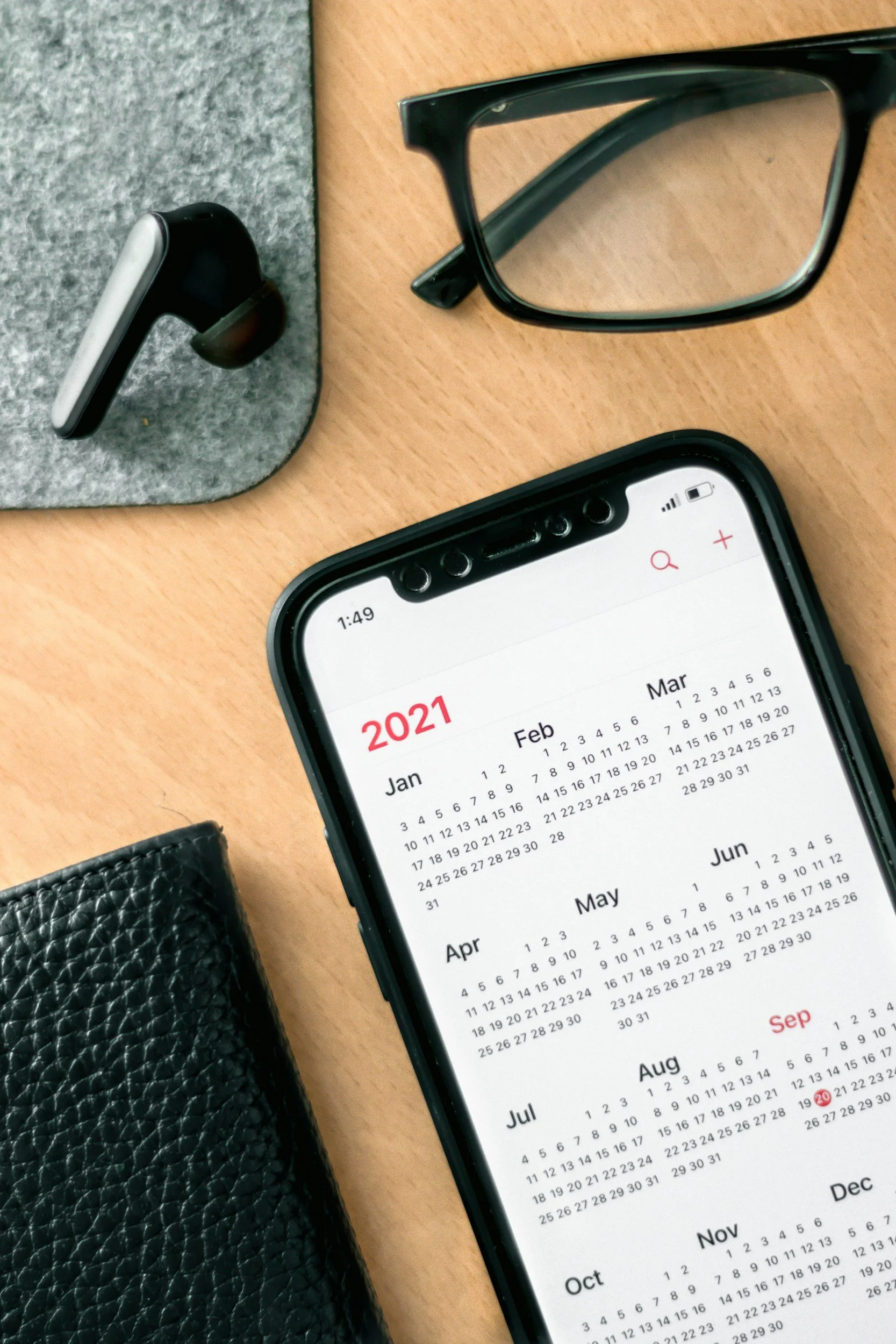 A smartphone displaying a 2021 calendar on its screen, preparing for a Mahoe Movement wellness also visible is a wireless earbud on top of a gray felt surface.