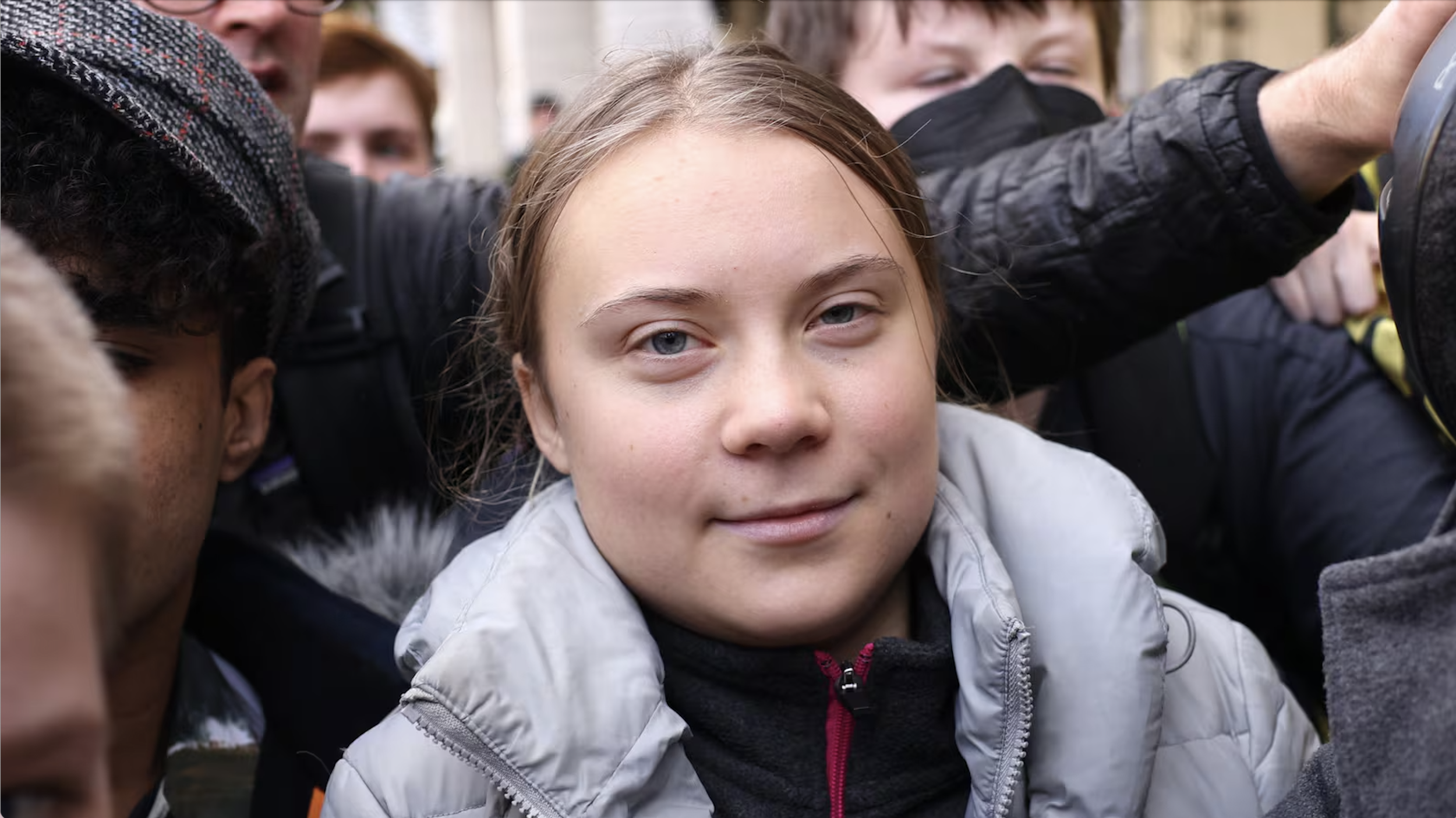 A young girl with light brown hair and blue eyes among a crowd of people, some of whom are wearing face masks.