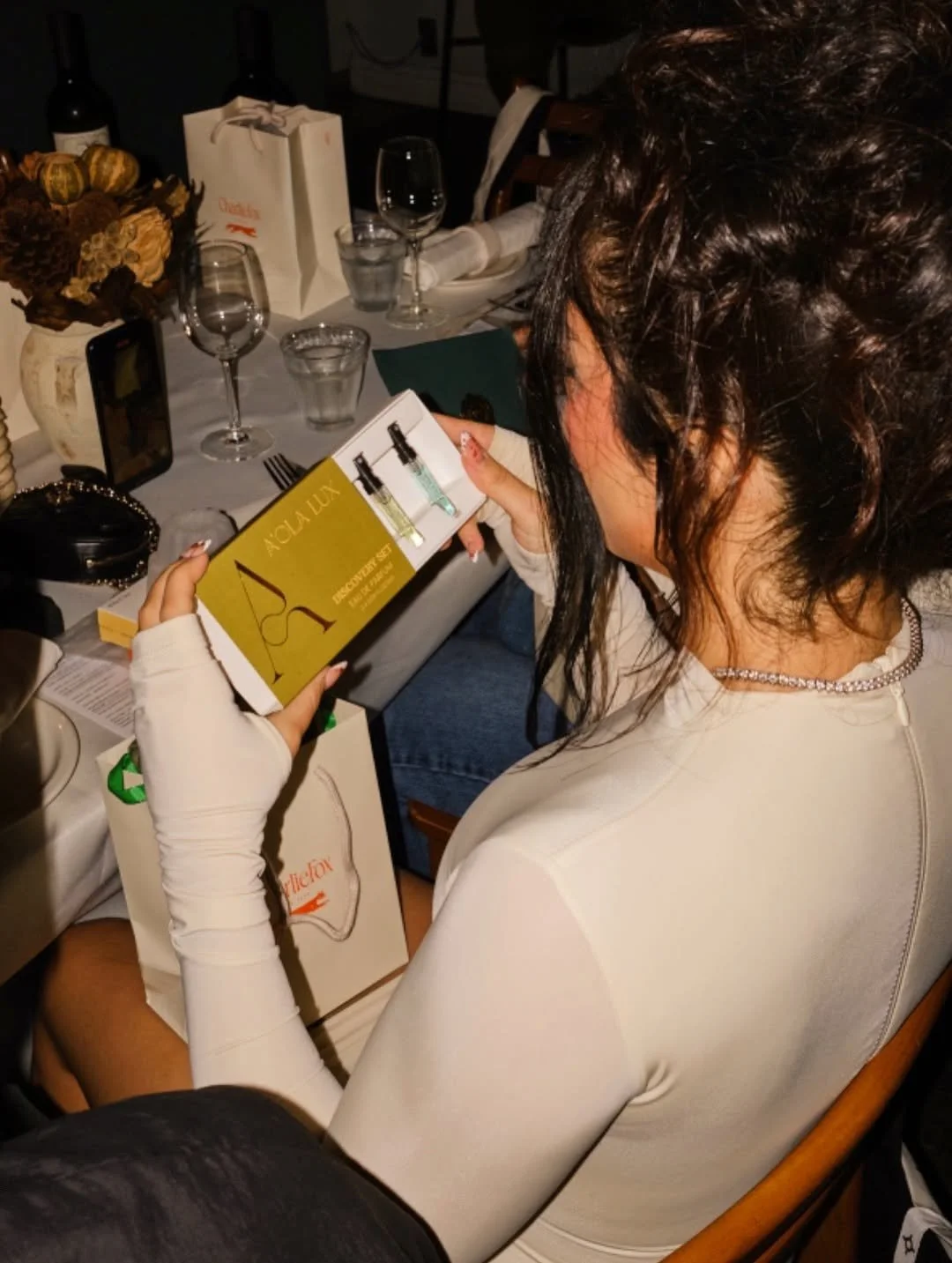 A woman sitting at a dining table looking at a box of perfume samples.