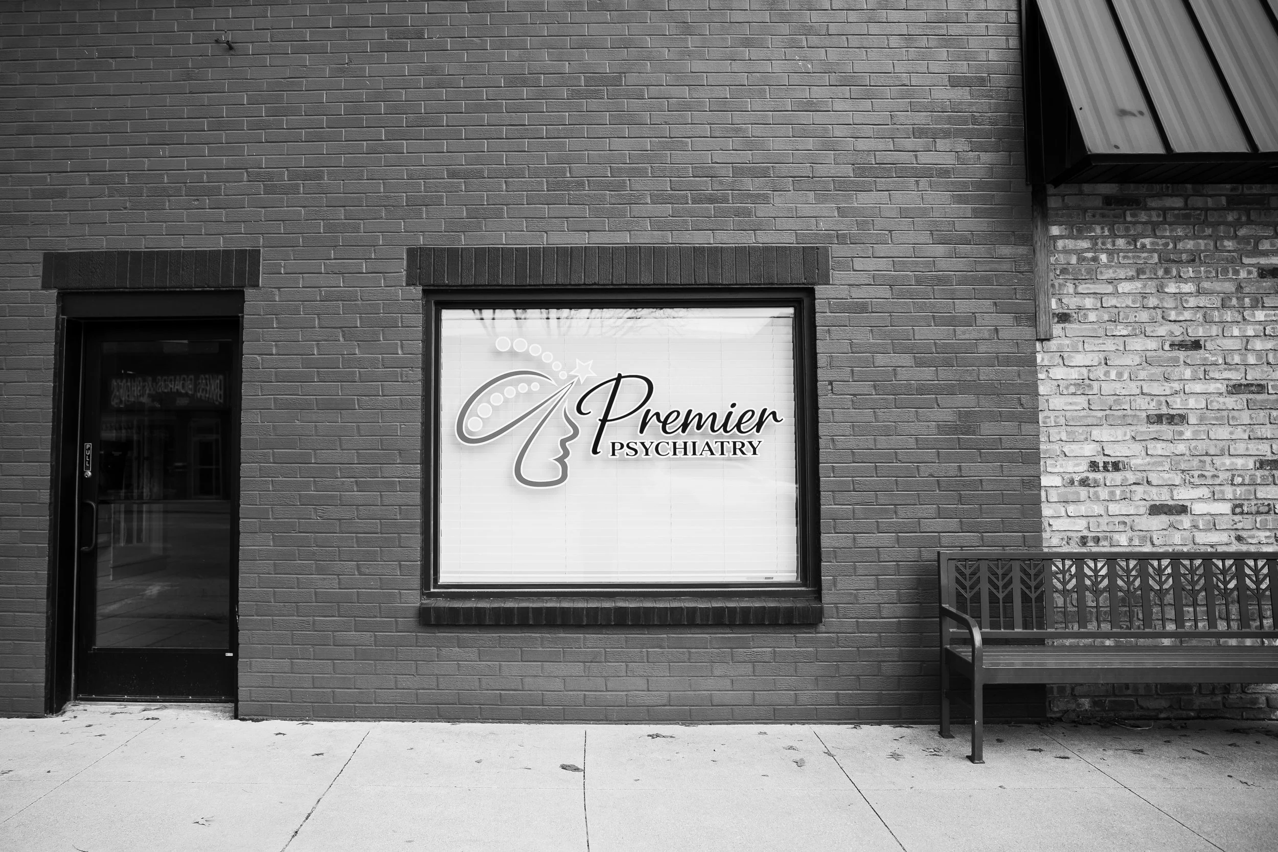 storefront with sign reading 'Premier Psychiatry,' a window, a door, a bench outside, and a sidewalk in black and white.