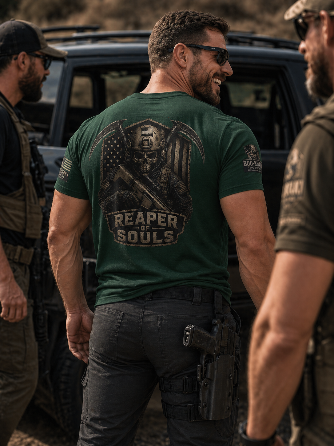 Group of men in tactical gear standing outdoors, with one man in the center wearing a green t-shirt with a skull logo and the words "Reaper of Souls," holding a gun holstered on his thigh, smiling, and wearing sunglasses.