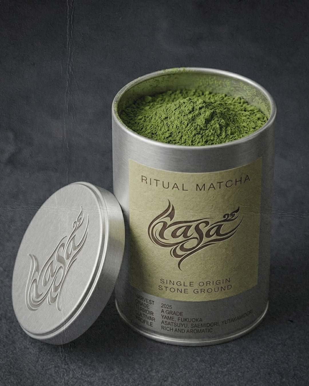 A metal container of vibrant green matcha powder with a matching lid beside it, labeled 'Ritual Matcha' and 'Kasa' with additional details about the product.