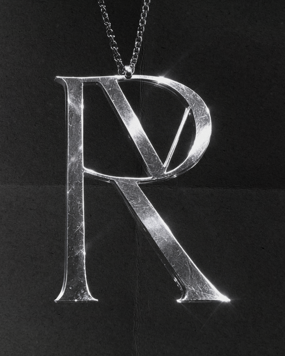 A silver necklace with a large, shiny letter R pendant hanging against a dark background.