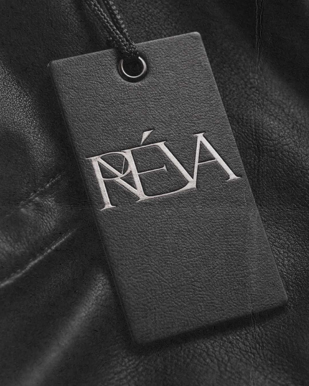 Close-up of a black leather item with a black tag displaying the text 'PRÉÁ' in white letters.